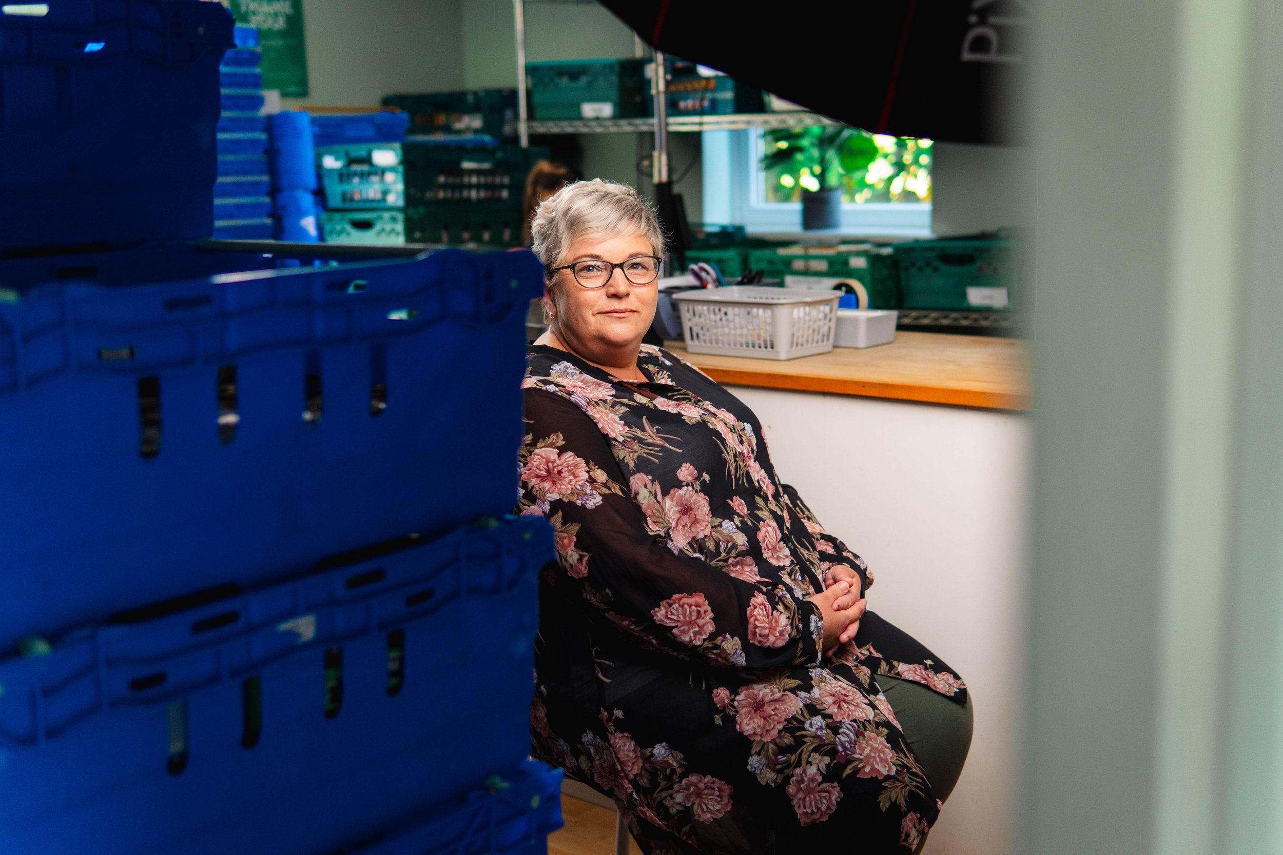 A young woman with red hair, blue eyes, and a nose ring smiling and resting her hand on her head.