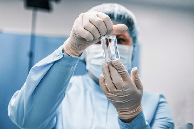 Pharmacist in a mask and cap inspecting an injectable vial