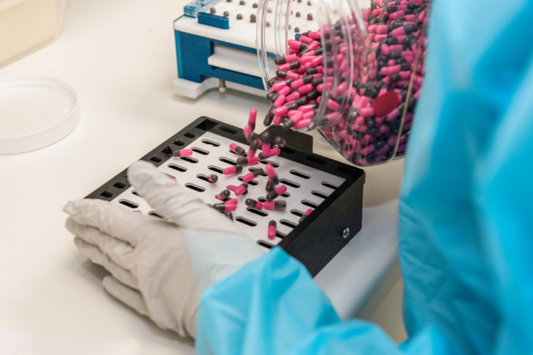 Gloved hands filling compounded capsules in a capsule machine