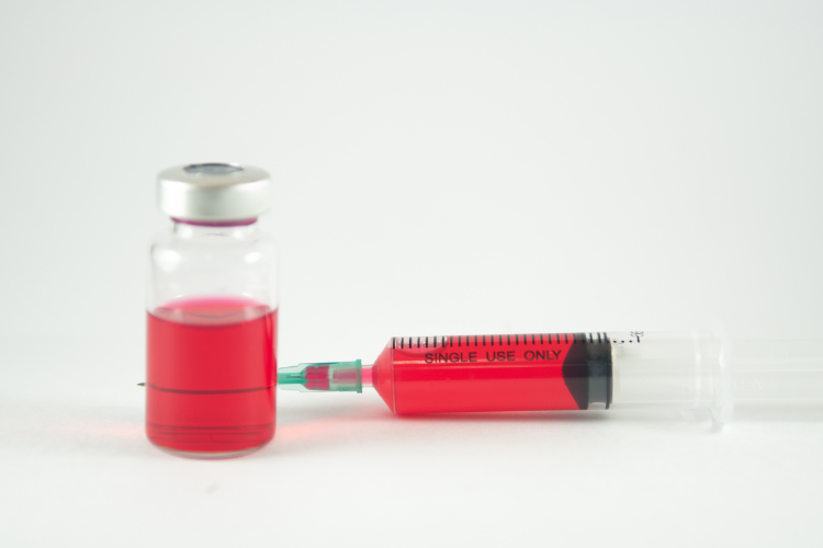 Glass vial of red vitamin B12 solution beside a filled syringe