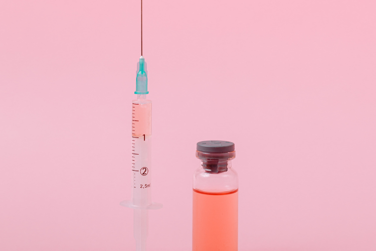 Syringe and vial of injectable medication on a pink background