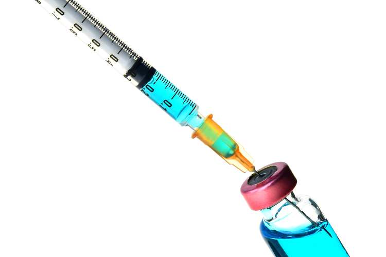 Syringe drawing liquid from a vial on a white background