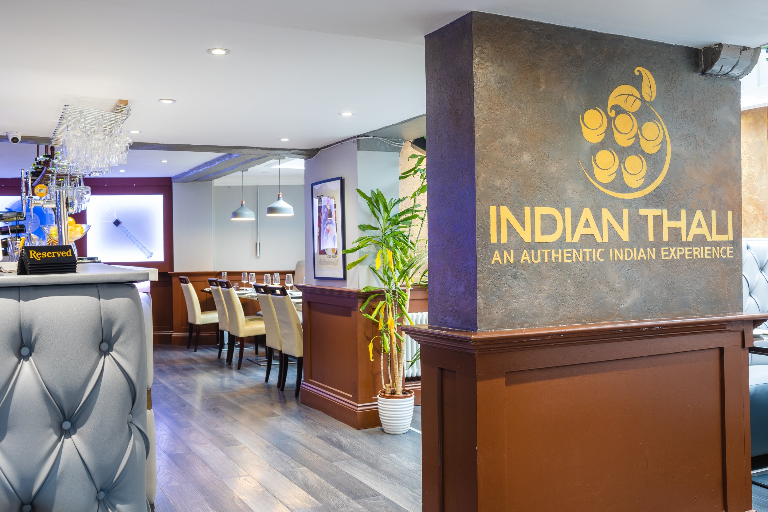 Interior of an Indian restaurant with a sign that reads 'INDIAN THALI - An Authentic Indian Experience' and features a chalkboard with a logo of a thali with various items.