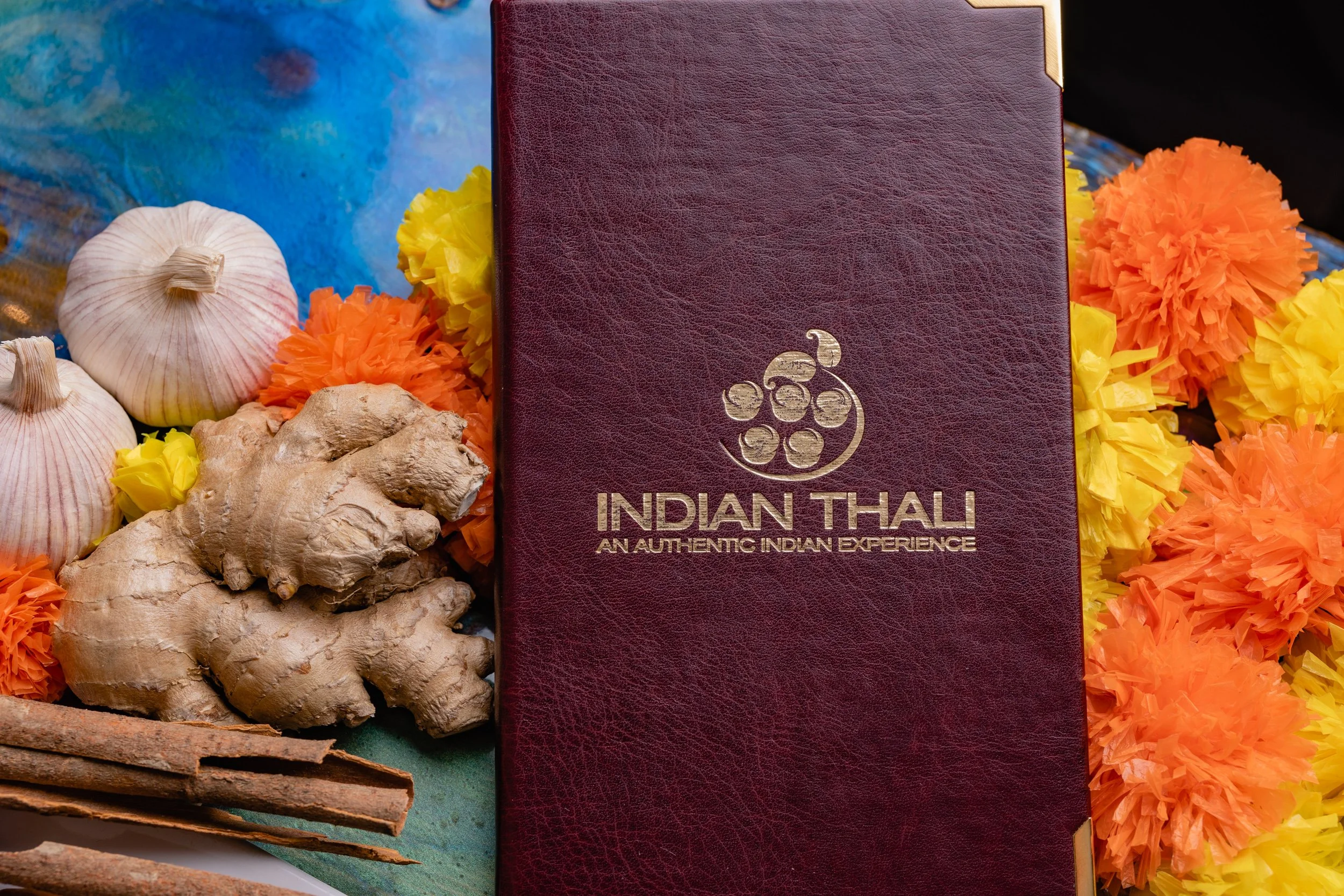 Menu titled Indian Thali surrounded by garlic, ginger, cinnamon, and orange and yellow paper flowers.