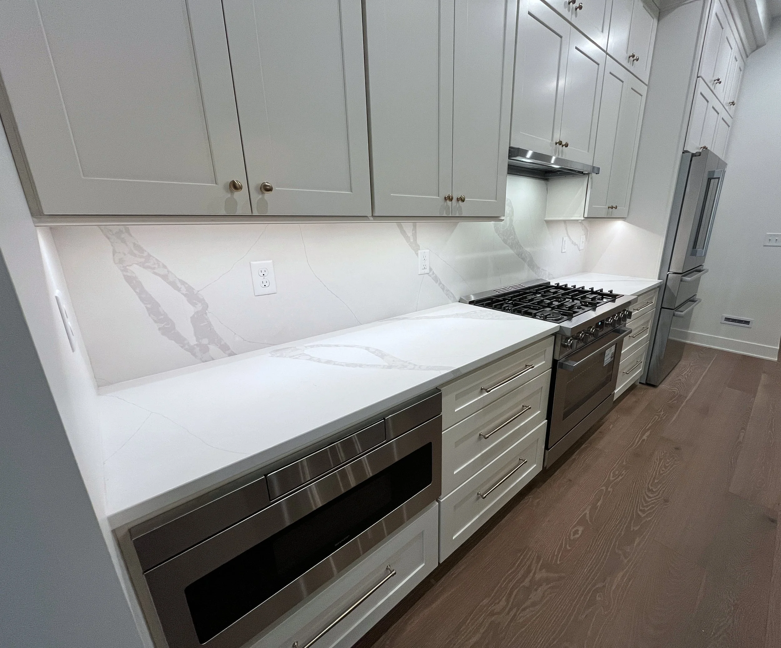 Modern kitchen with white countertops, gray cabinets, stainless steel appliances, and hardwood flooring. We specialize in Granite, Quartz, and Marble Countertops. Free Quotes available. Custom Countertops. Northwest Indiana, Chicagoland, Illinois
