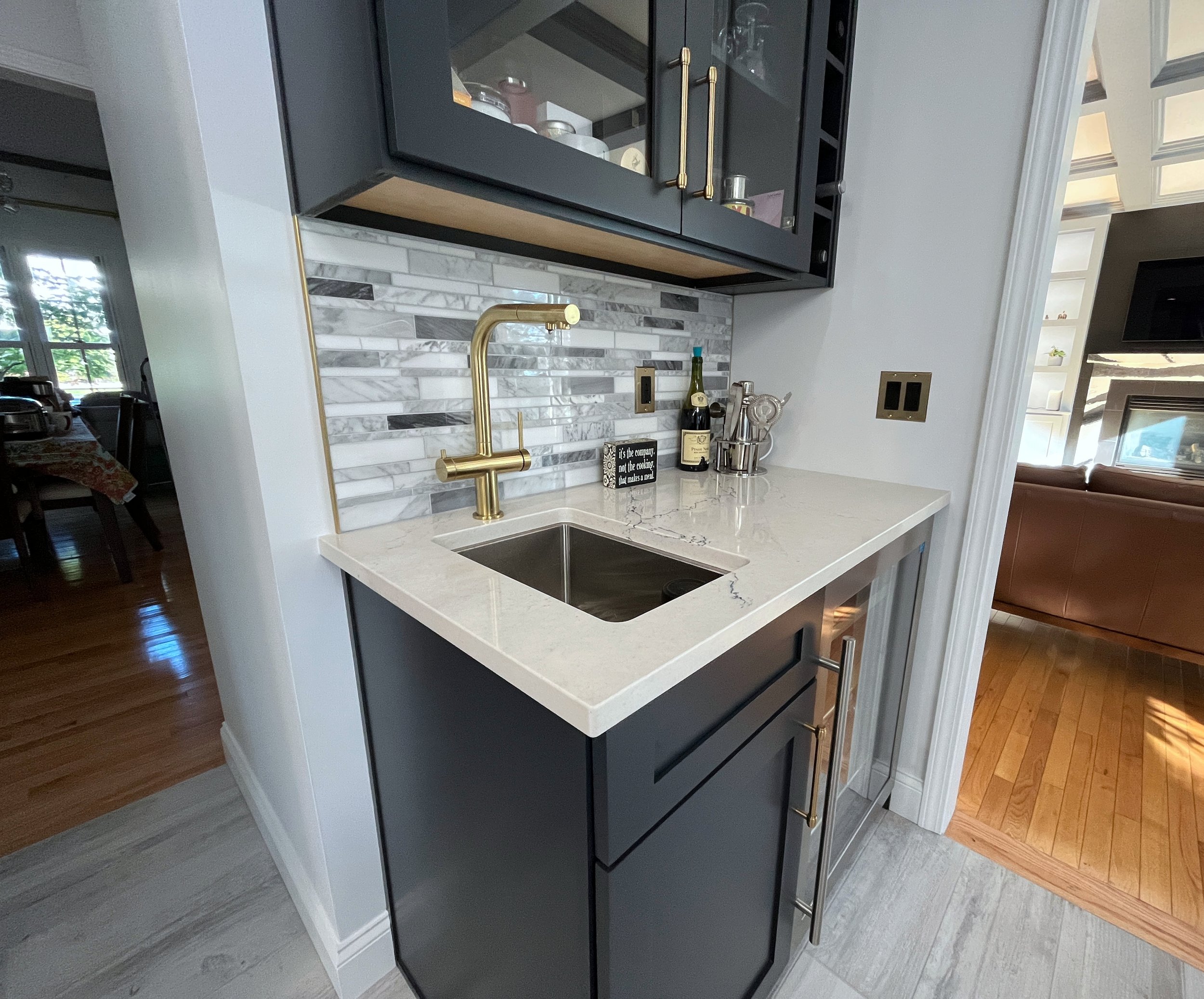 A modern kitchen with a black cabinet, brass handles, marble backsplash, and white countertop with a gold faucet. We specialize in Granite, Quartz, and Marble Countertops. Free Quotes available. Custom Countertops. Northwest Indiana, Chicagoland
