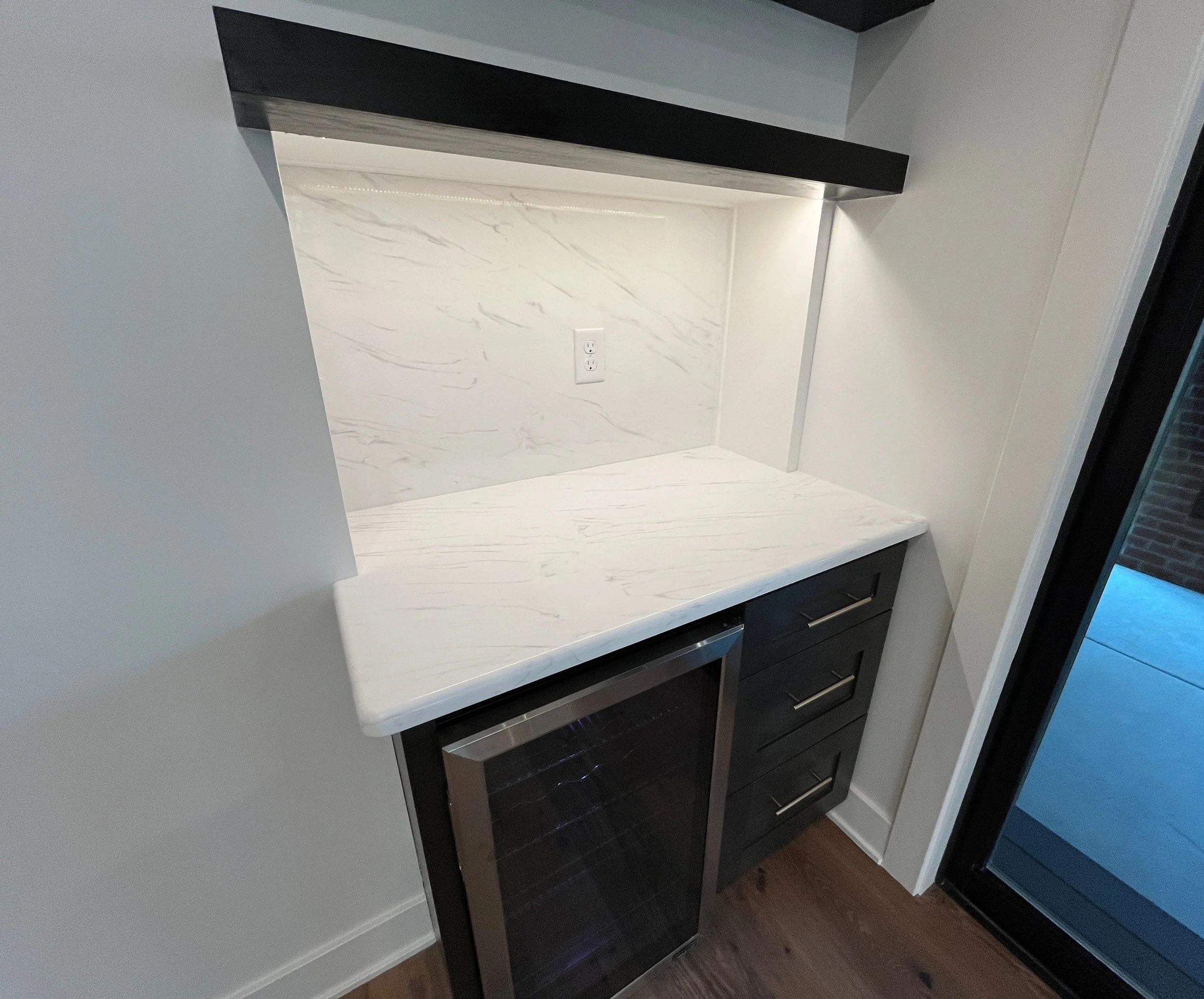 A modern bathroom vanity setup with a white marble countertop, dark wooden cabinets with horizontal handles, an electrical outlet, and a marble backsplash with gray veining. We specialize in Granite, Quartz, and Marble Countertops. Free Quotes.