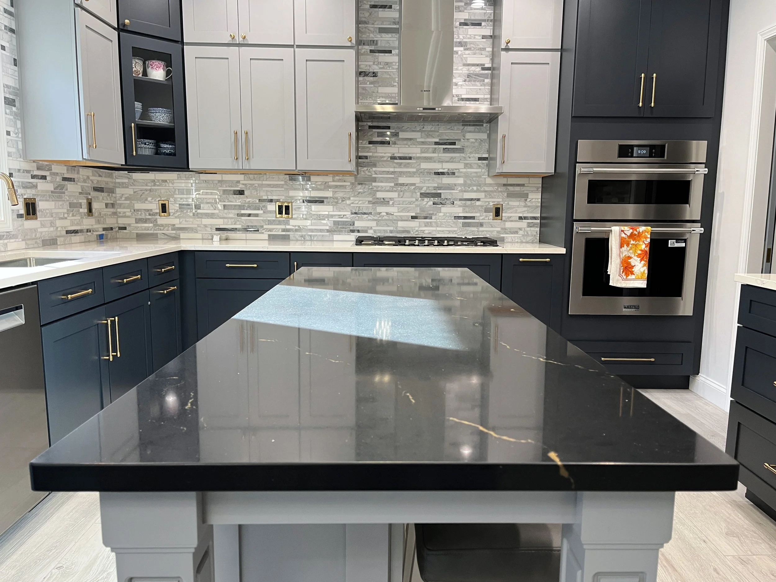 Modern kitchen with black and white cabinets, marble backsplash, stainless steel oven, and black countertop island. We specialize in Granite, Quartz, and Marble Countertops. Free Quotes available. Custom Countertops. Northwest Indiana, Chicagoland