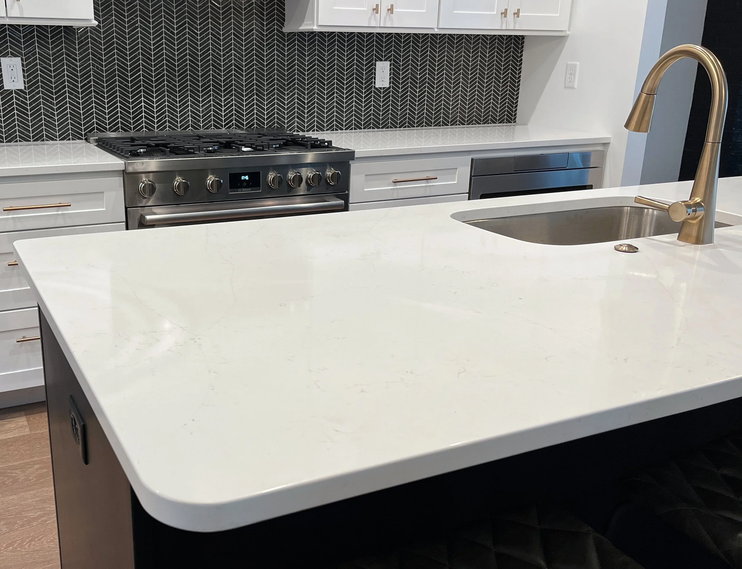 Modern kitchen with a white marble island, black subway tiling backsplash, stainless steel gas range, and white cabinets with gold handles. We specialize in Granite, Quartz, and Marble Countertops. Free Quotes available. Custom Countertops. Northwest