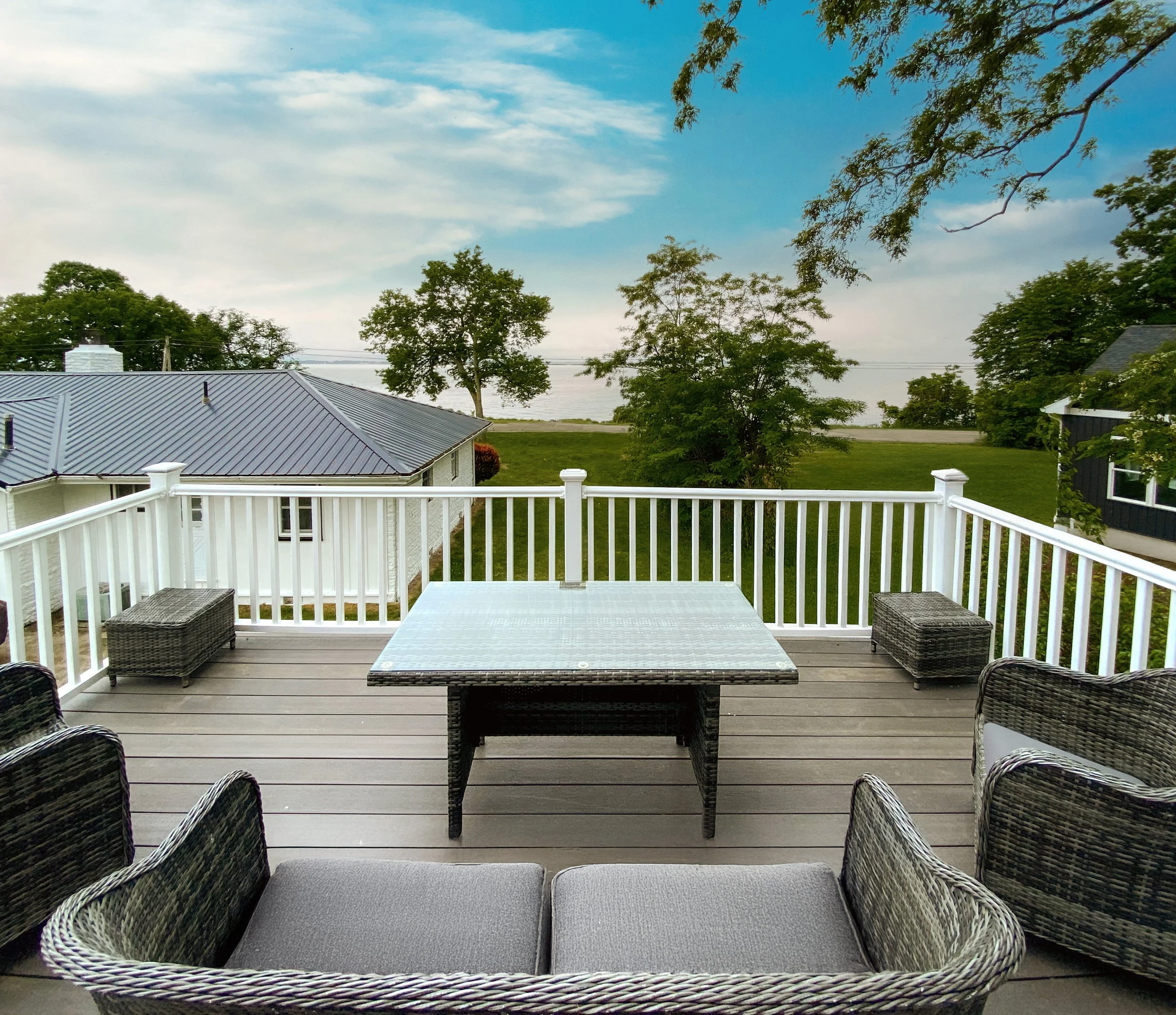 View from a balcony with outdoor furniture overlooking trees and a body of water under a partly cloudy sky.