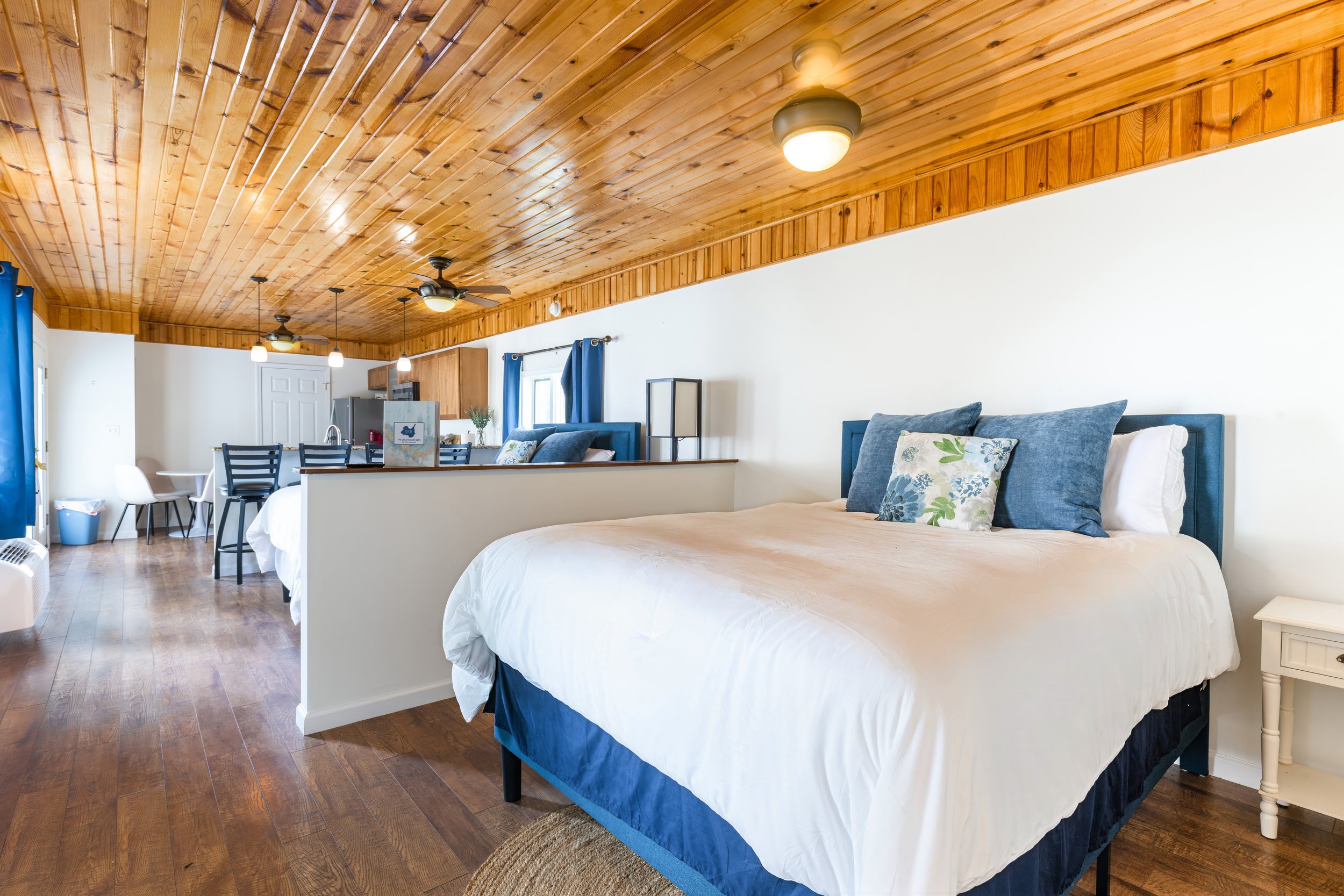 A bedroom with a wooden ceiling, a ceiling fan, and a bed with blue pillows and white bedding.