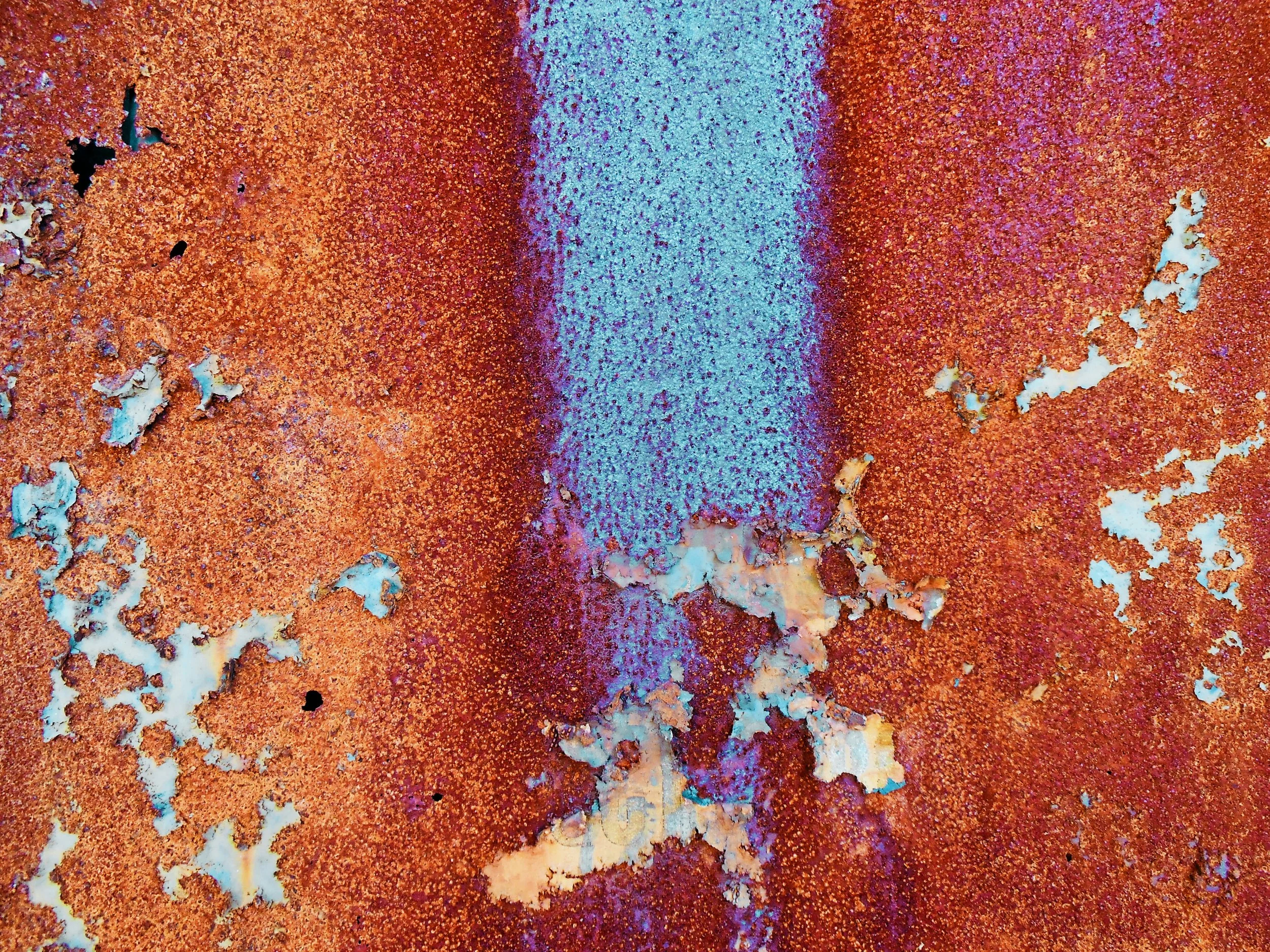 Close-up of a rusty, peeling metal surface with orange and purple hues.