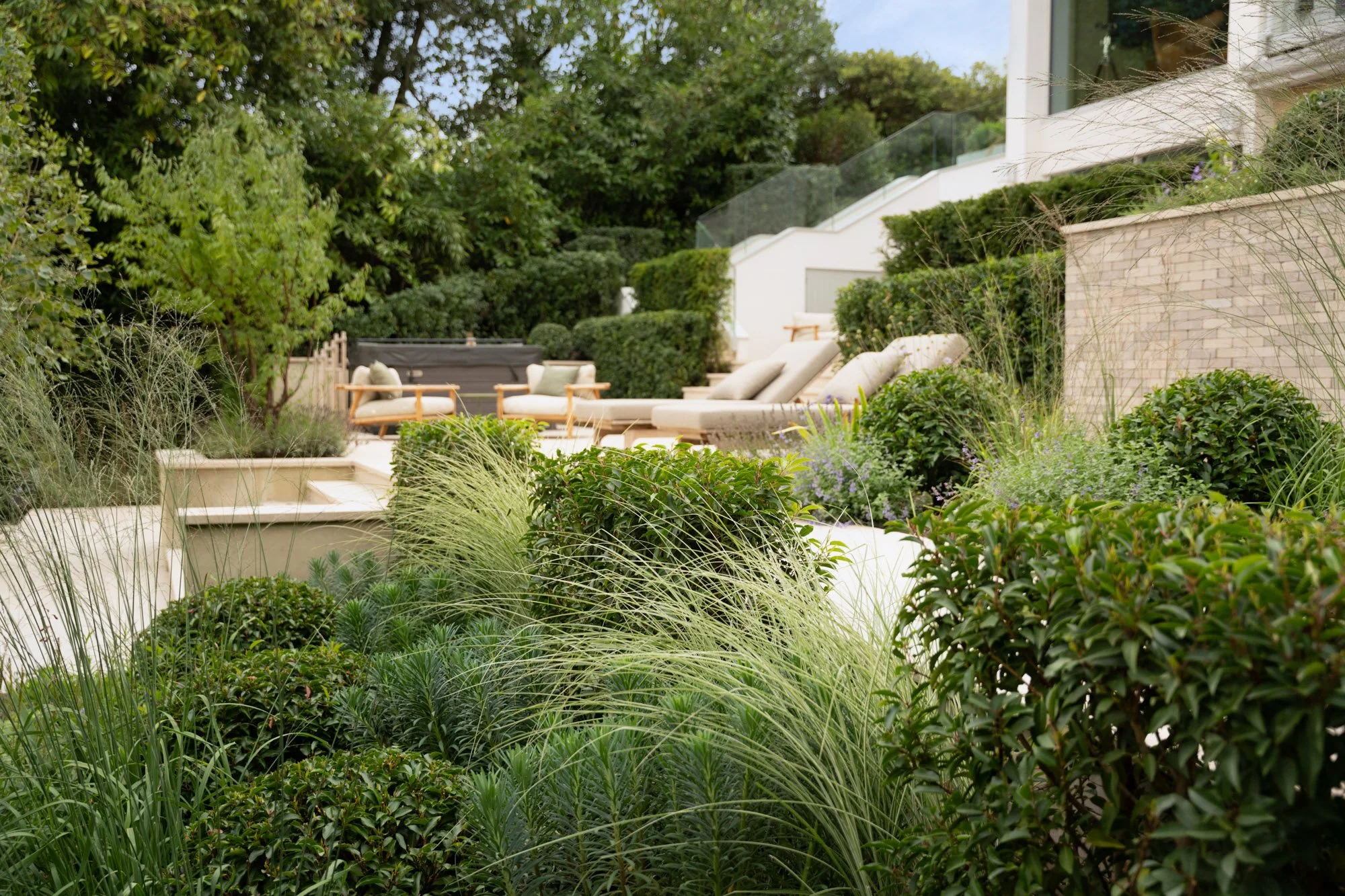 Lush backyard garden with seating area, lounge chairs, and various plants and shrubs on a hillside.