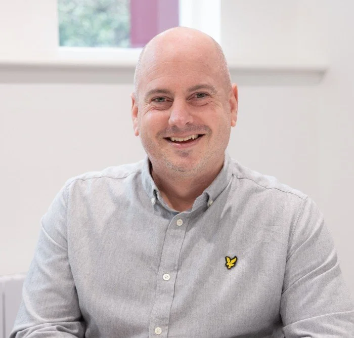 Smiling man in a light gray shirt sitting indoors
