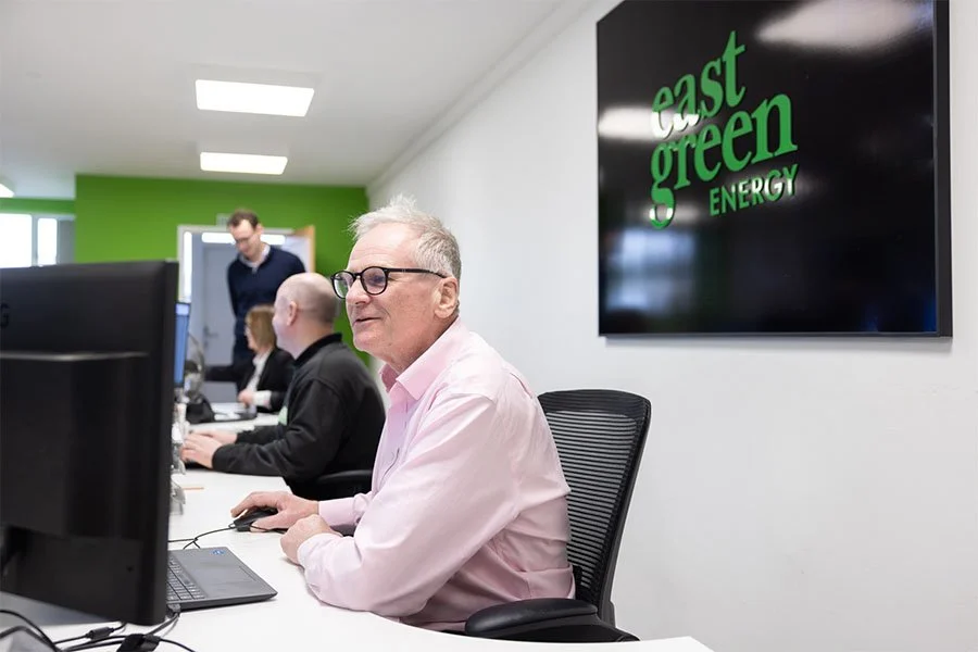 Office with people working at computers, "East Green Energy" sign on wall.