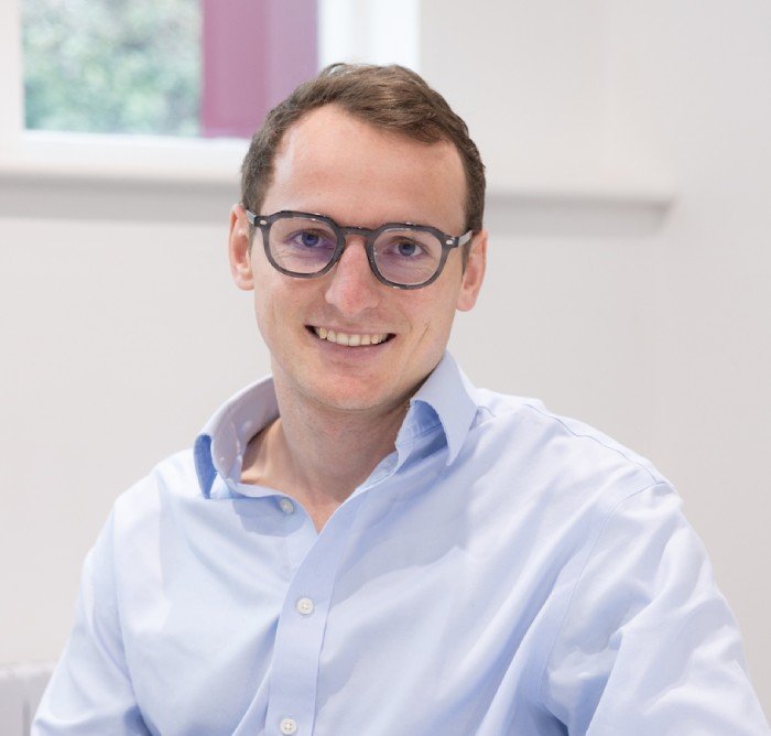 Person wearing glasses and a blue shirt, smiling in an indoor setting.