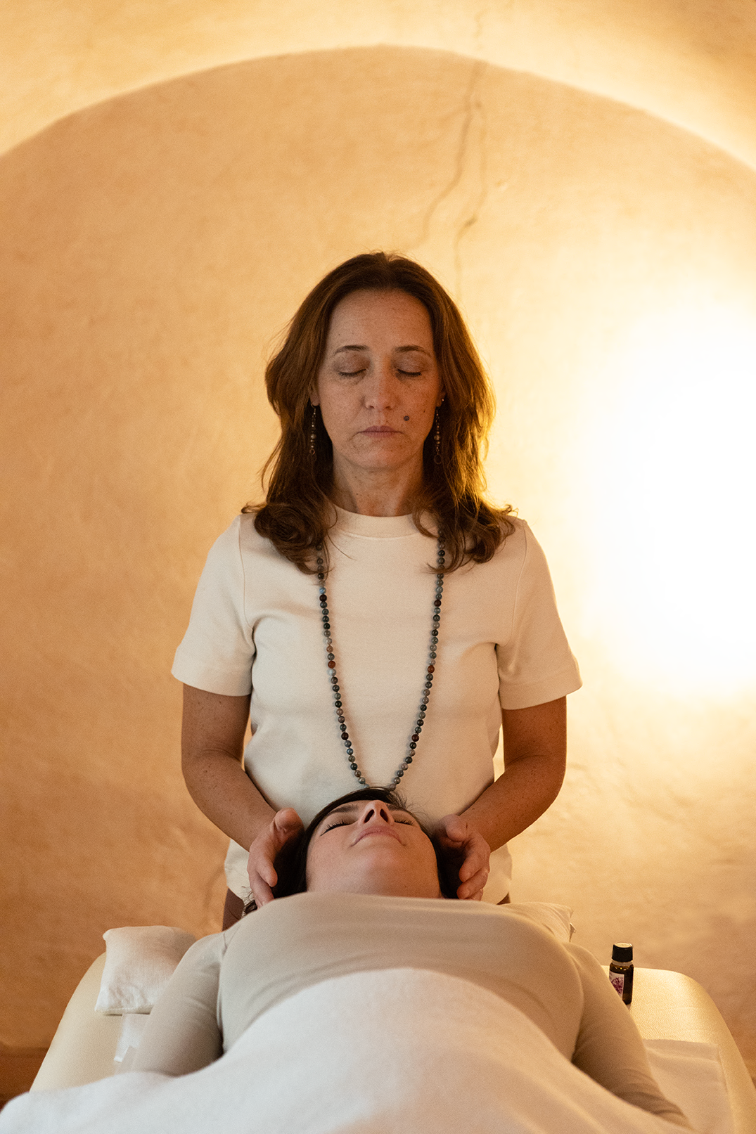 Una donna che riceve un massaggio alla testa in un ambiente tranquillo, con luci soffuse e pareti beige.