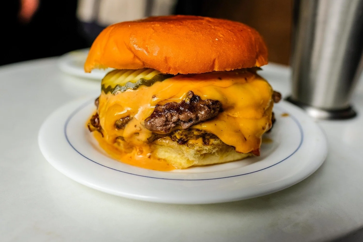 Close-up of cheeseburger with melted cheddar cheese, pickles, beef patty, on a white plate