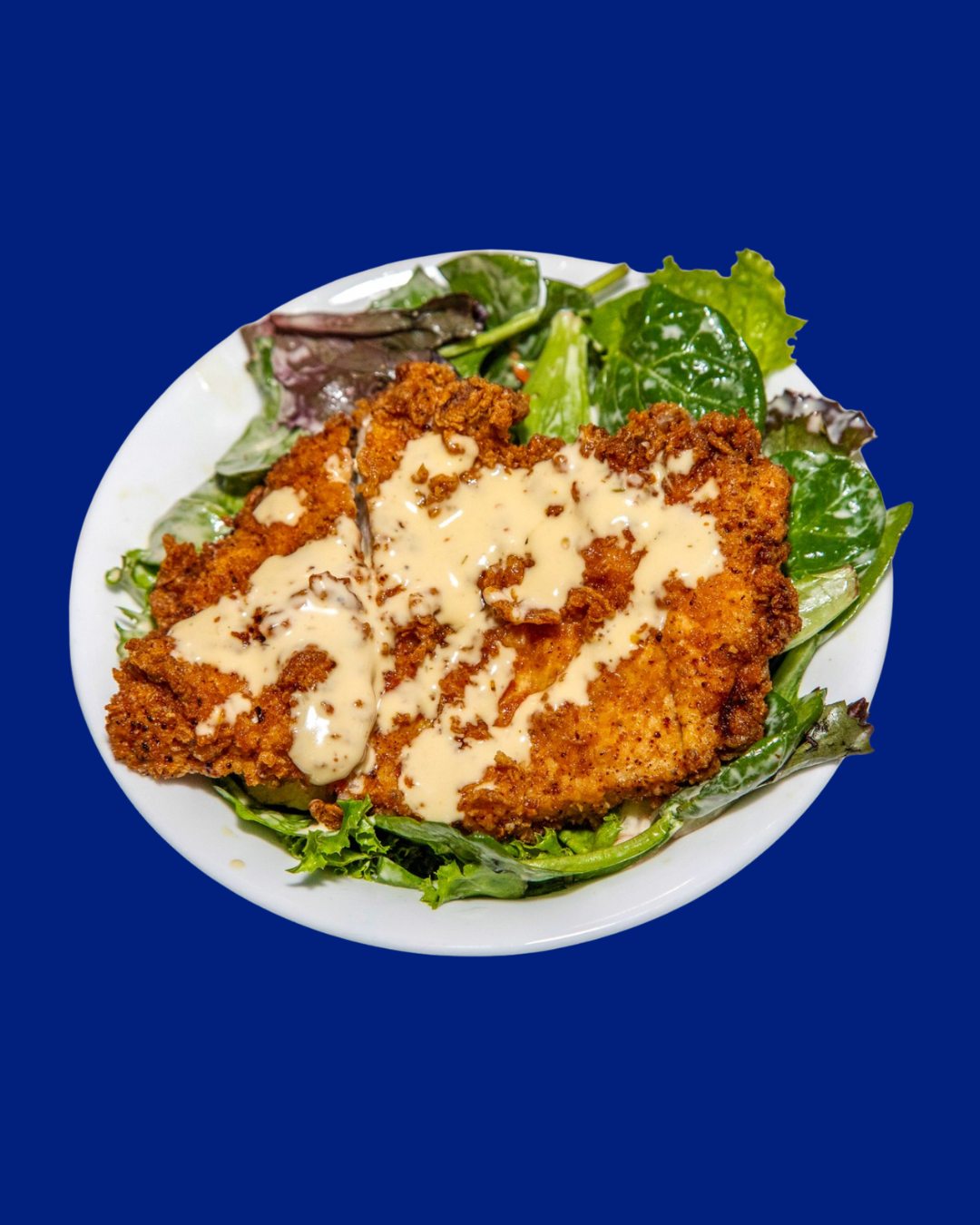 Bowl of fried chicken breast topped with creamy dressing, served on a bed of mixed greens salad.