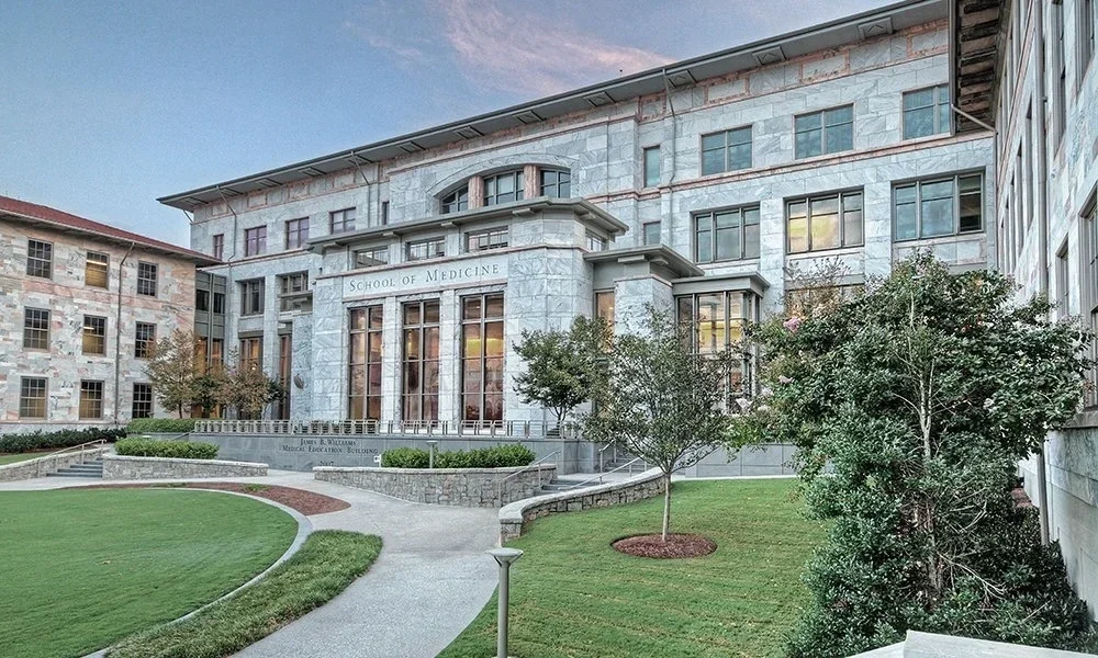 Exterior of a medical school building with a sign that reads "School of Medicine" and surrounding landscaped lawn.
