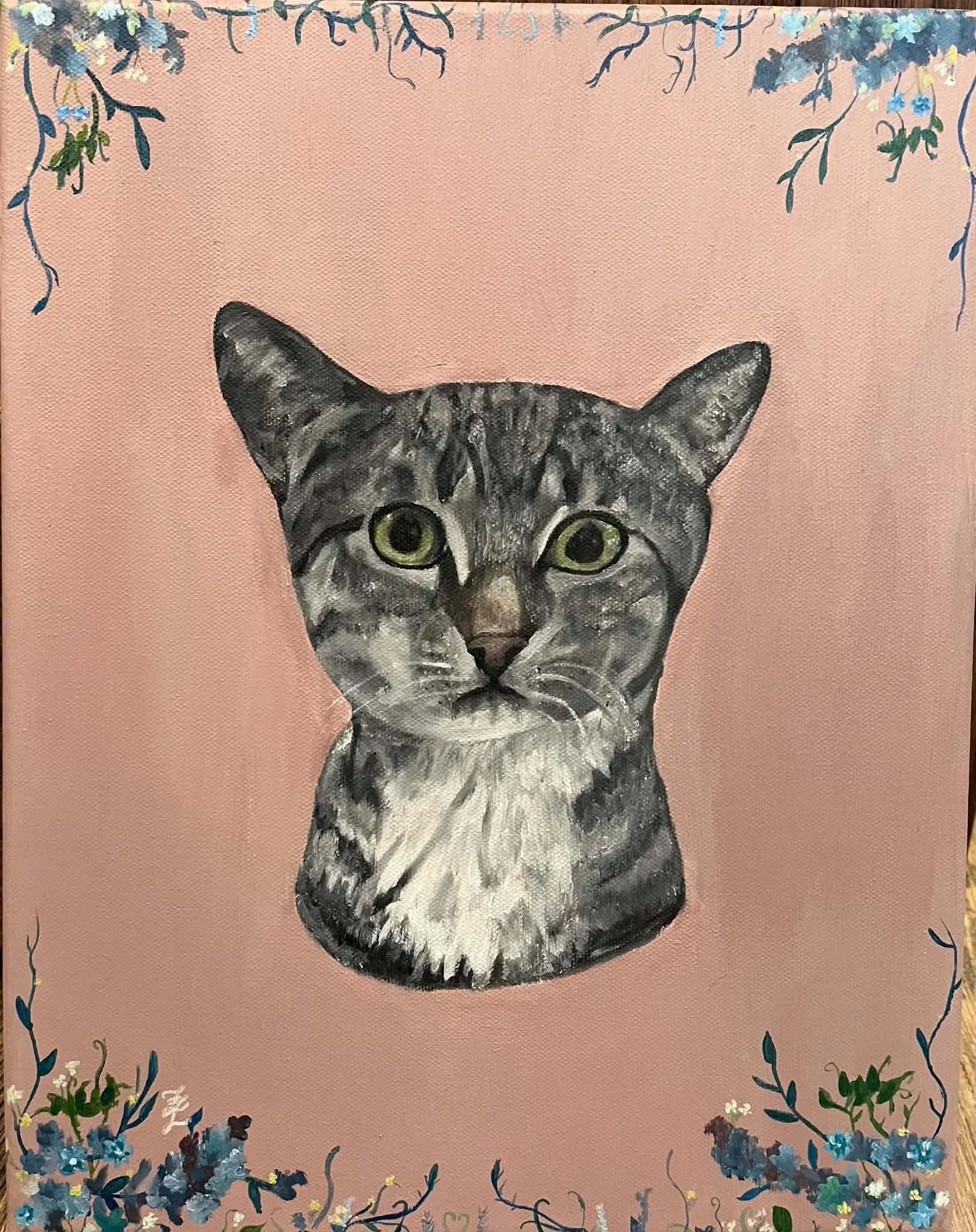 A painting of a gray tabby cat with green eyes on a pink background, decorated with blue and white flowers and green stems around the border.
