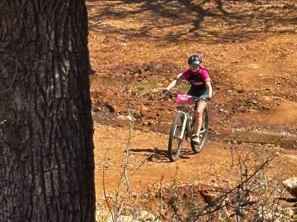 A Femmes rider in a pink jersey riding down a red dirt trail