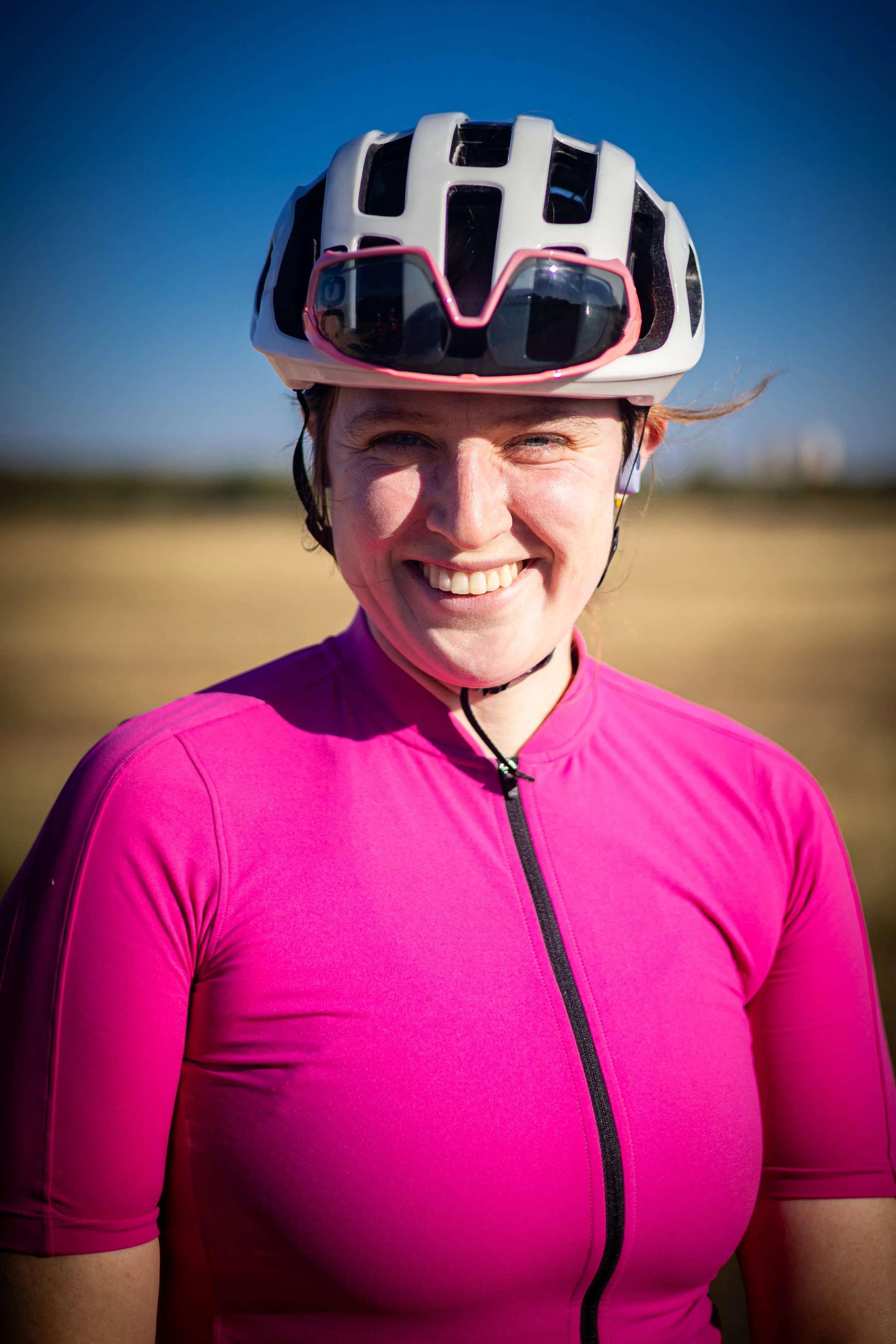 Woman riding a mountain bike outdoors with a helmet and sunglasses on a sunny day.