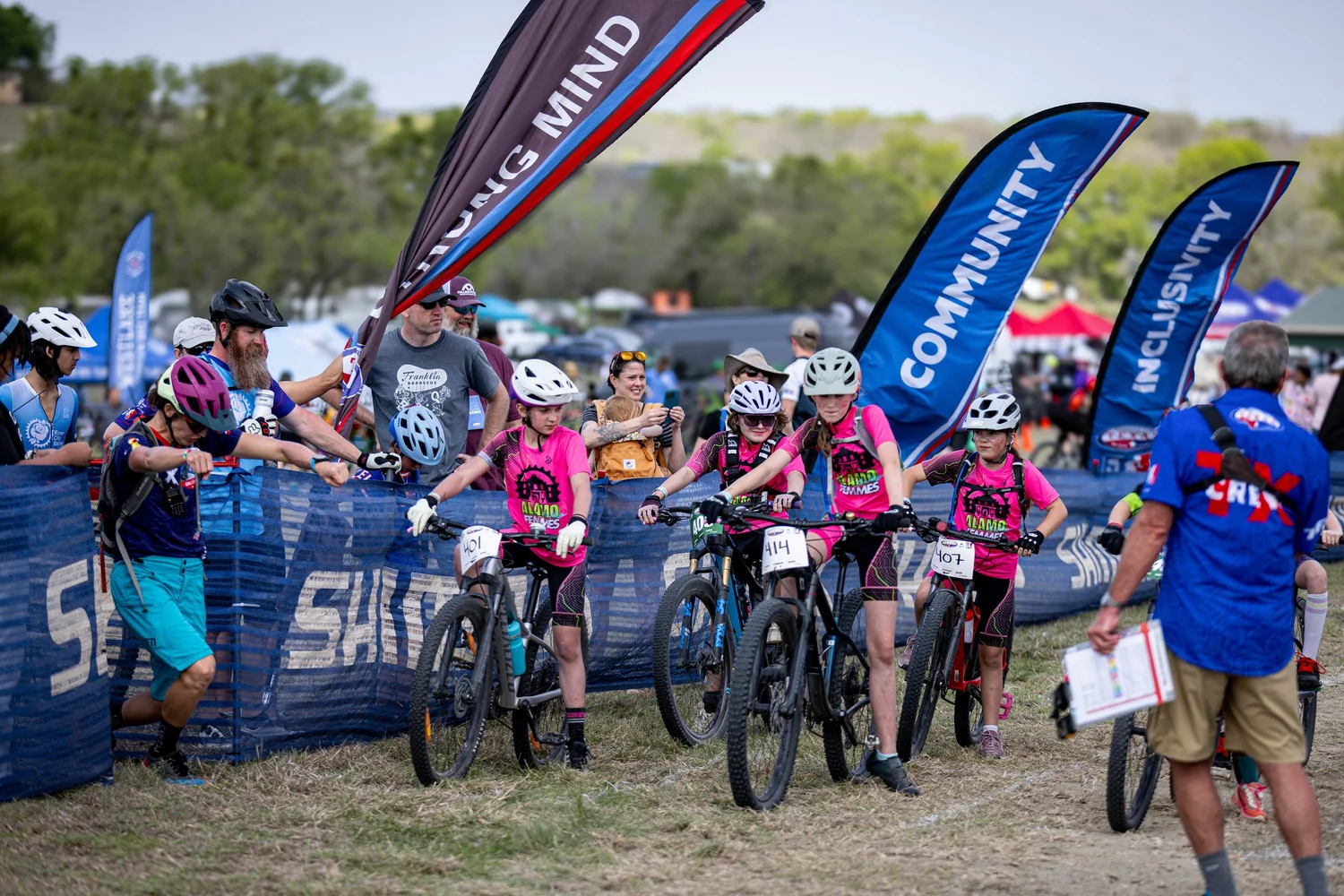 Riders lined up at the start of a Texas NICA race with sponsor flags behind them