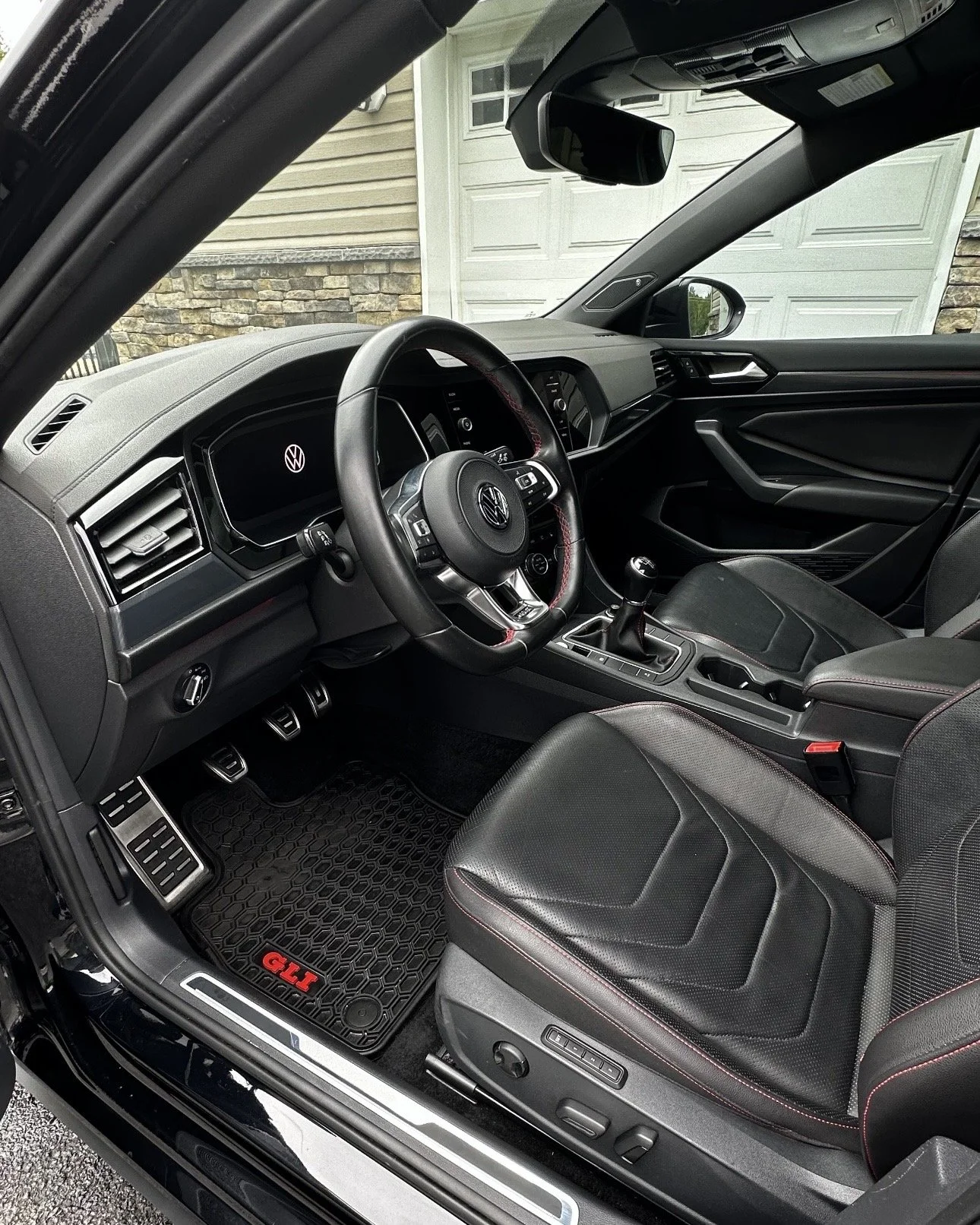 Interior of a Volkswagen car showing the dashboard, steering wheel, gear shift, driver's seat, and floor mats with the 'GTI' logo.