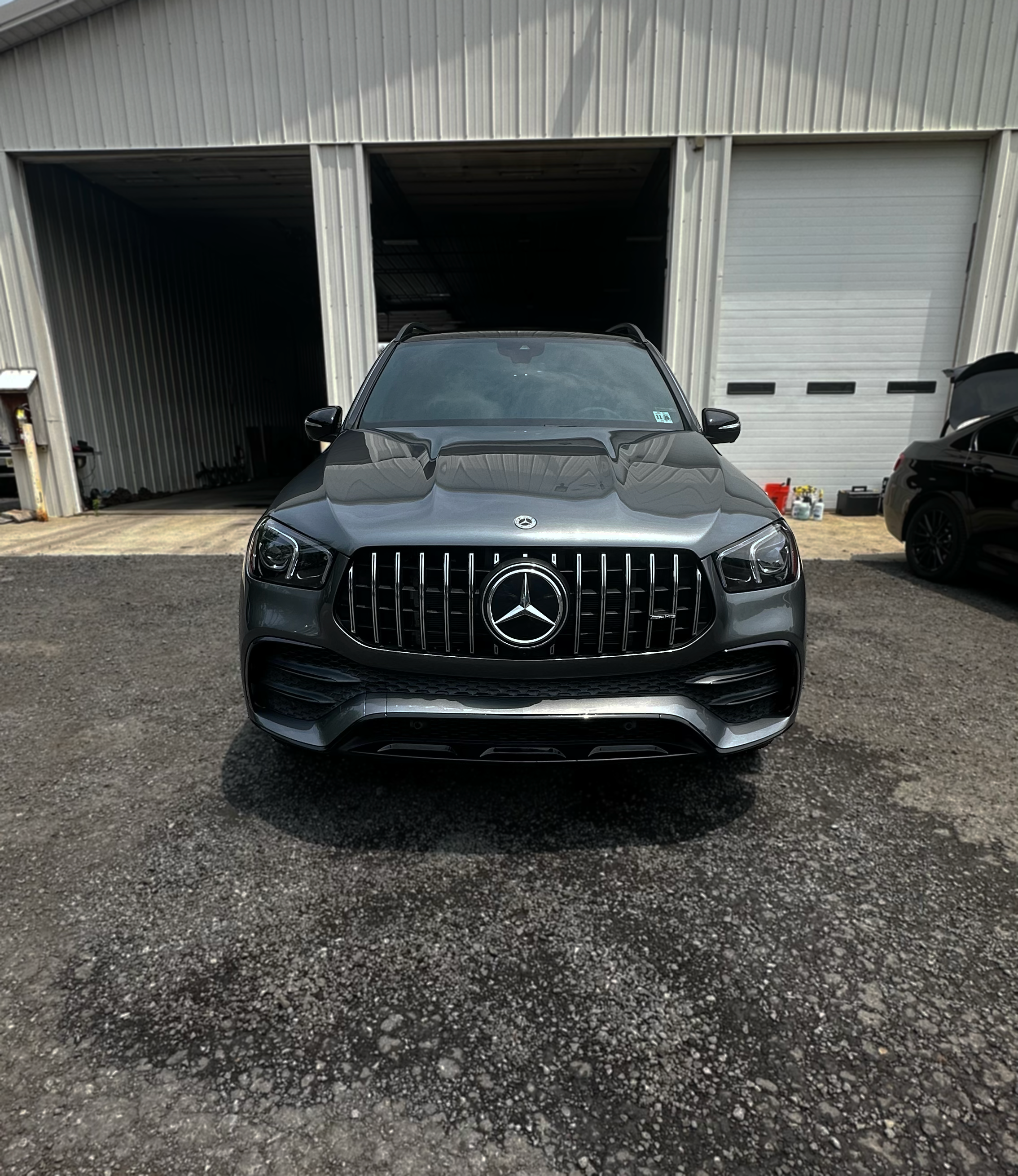 Front view of a silver Mercedes-Benz SUV parked outside a metal industrial building with three large garage doors.