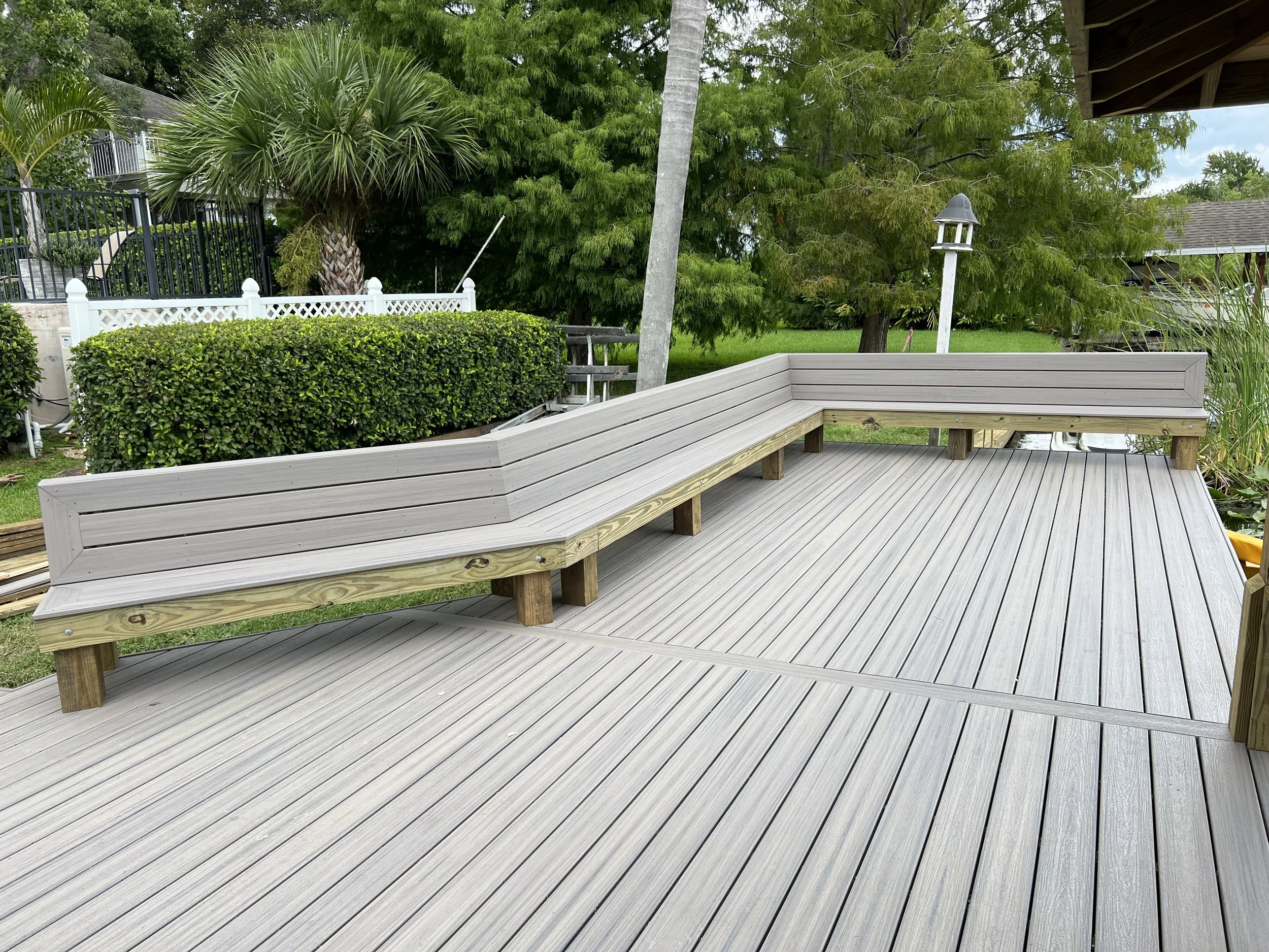 A wooden deck with built-in seating area near a pond with surrounding greenery, custom built seating built into deck by local dock builder.