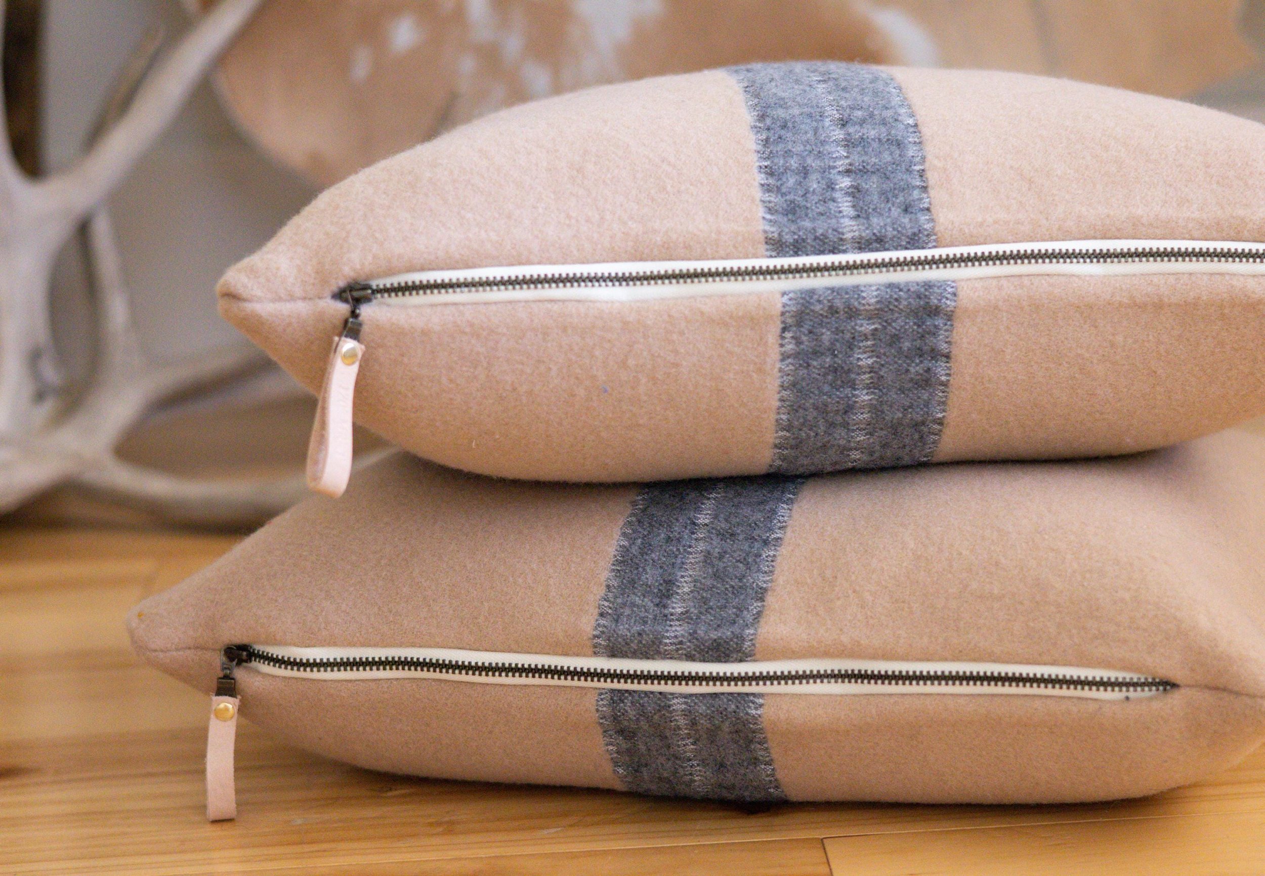 Beige and gray stripe Pendleton® wool pillows laid on the side showcasing a leather pull zipper