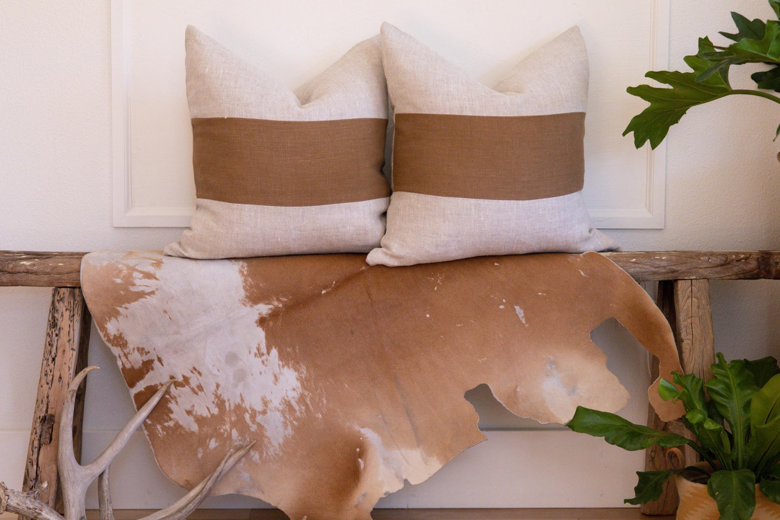 Two Caramel Block Stripe Beige Linen Pillow Cover sitting side by side on a wooden bench
