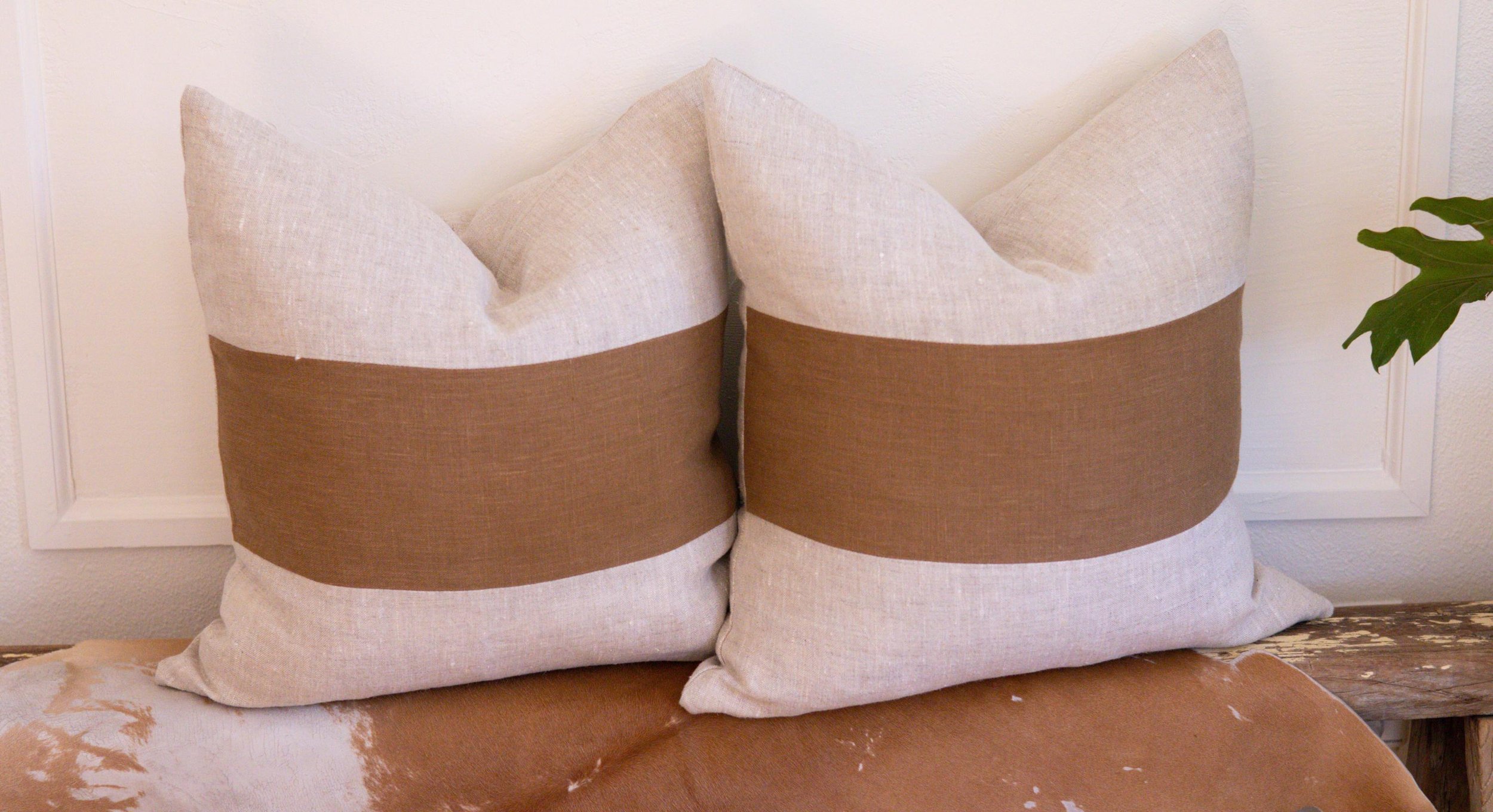 Close up of Two Caramel Block Stripe Beige Linen Pillows by Pine and Wool Home sitting side by side on a wooden bench