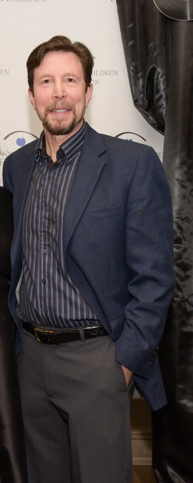 Man in blue blazer and striped shirt standing indoors