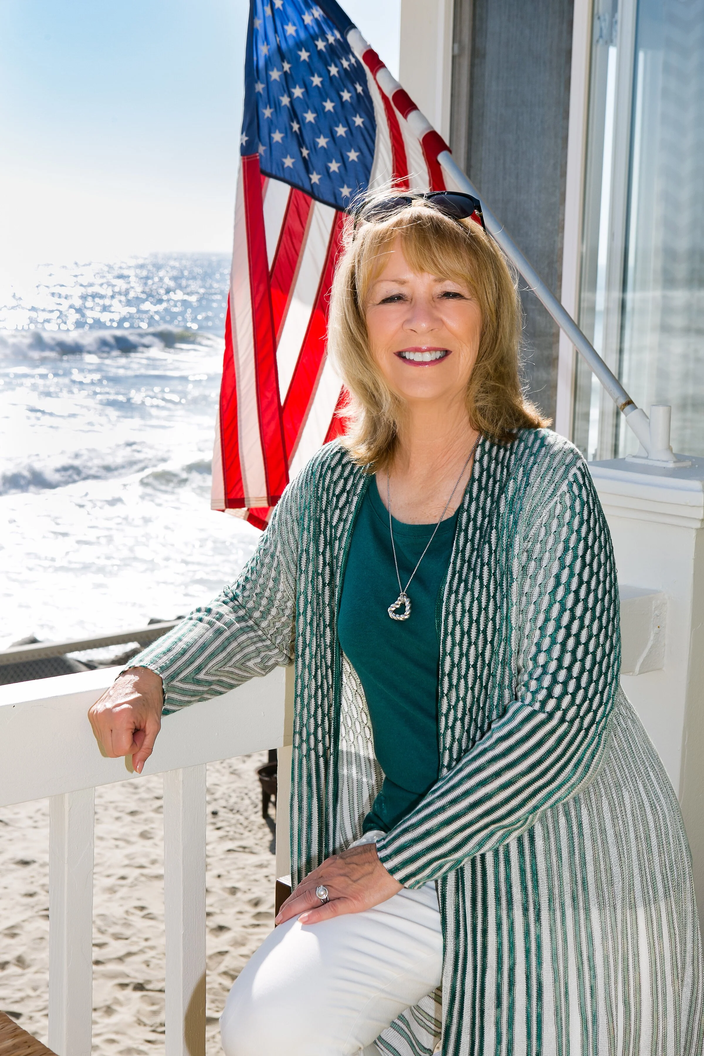 Smiling woman on a beachside porch with an American flag.