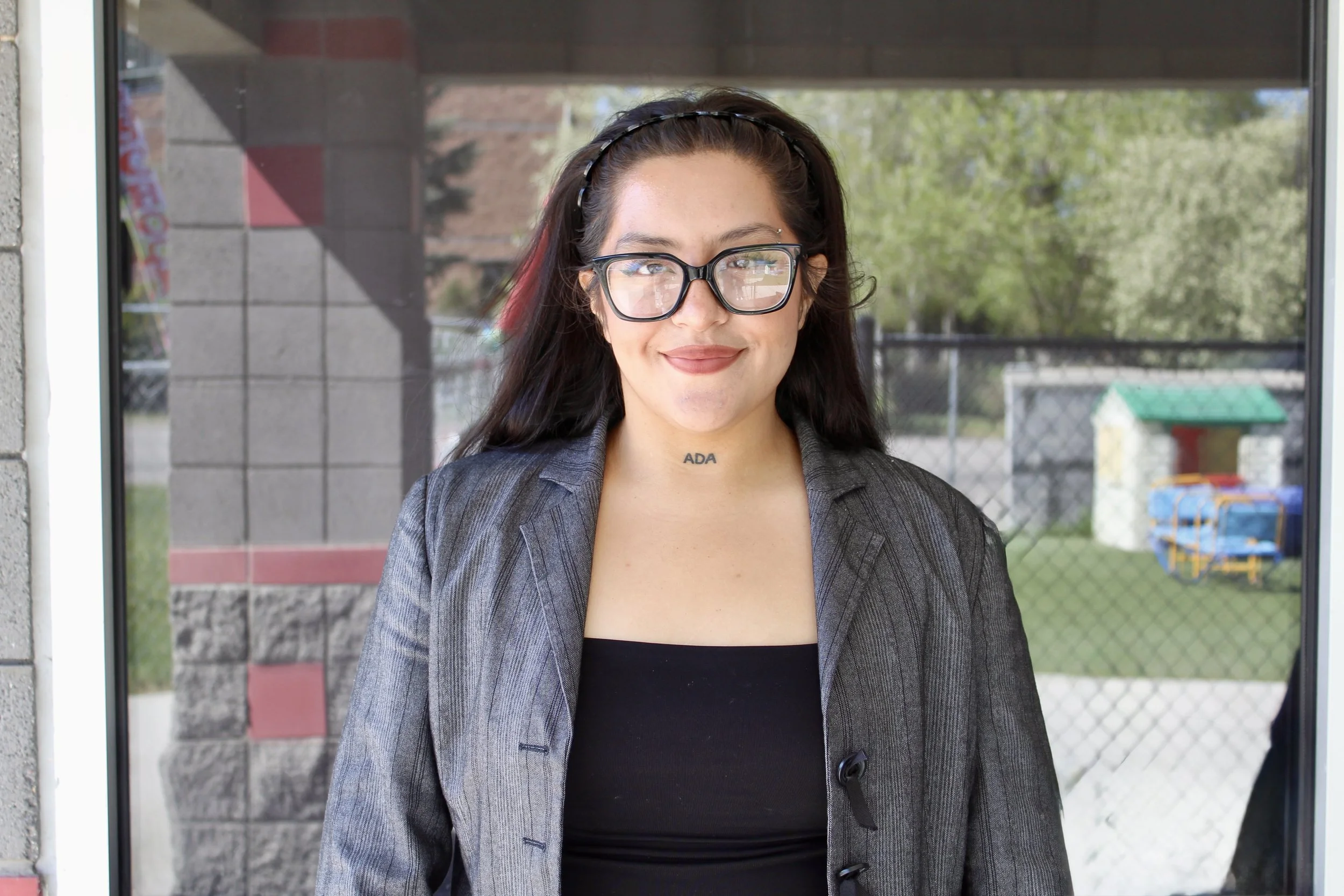 Person wearing glasses and a formal jacket, standing outdoors.