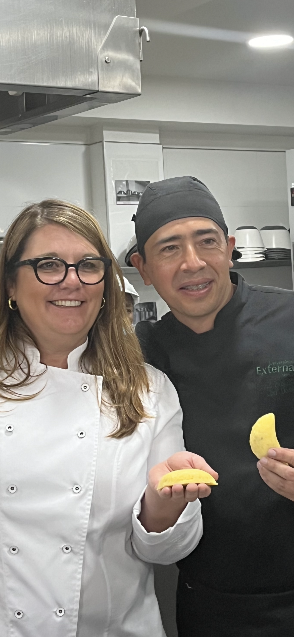 A female chef and a male chef standing together in a commercial kitchen, each holding a half of a yellow lemon.