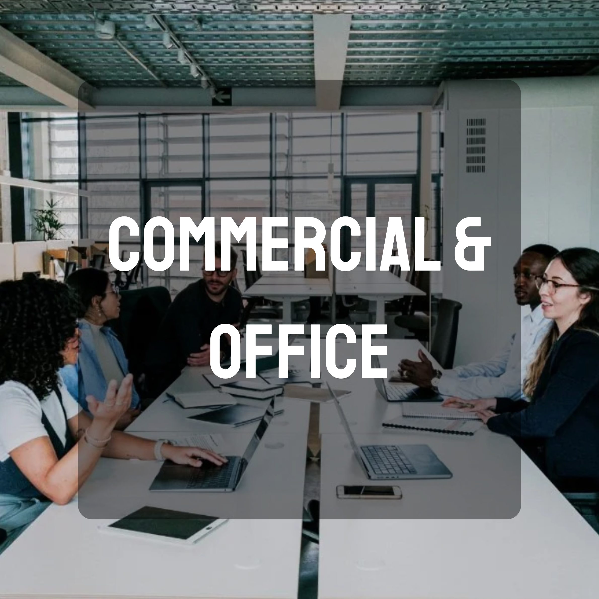 A group of people sitting around a conference table in an office, engaging in a discussion, with laptops and documents in front of them.