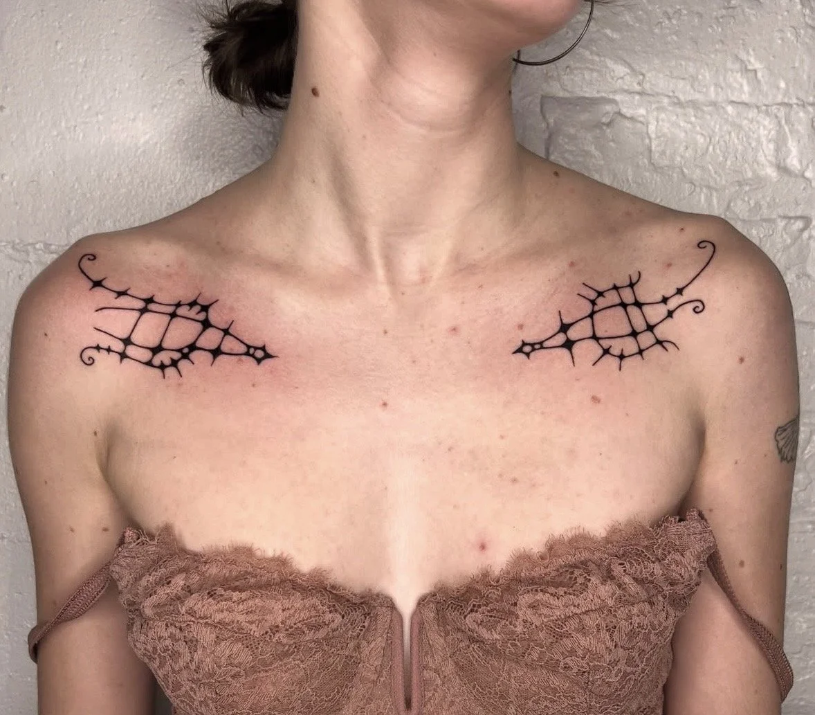 Tattooed black web-like designs on woman's shoulders.
