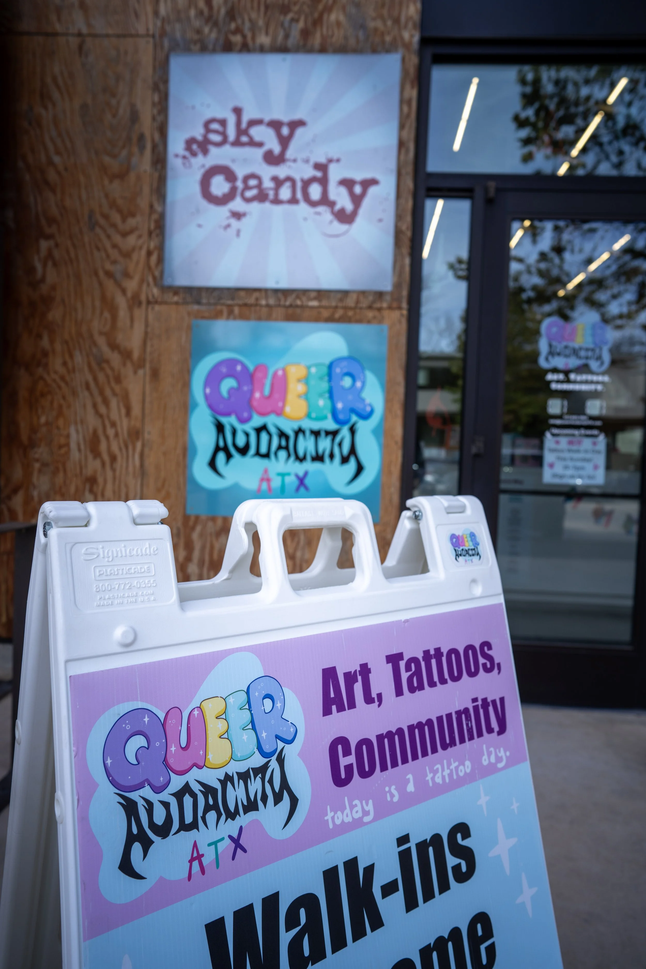 photo of a store front. There are two signs for businesses, one for Sky candy austin: an areal arts gym, and one for Queer Audacity ATX, a queer tattoo studio.