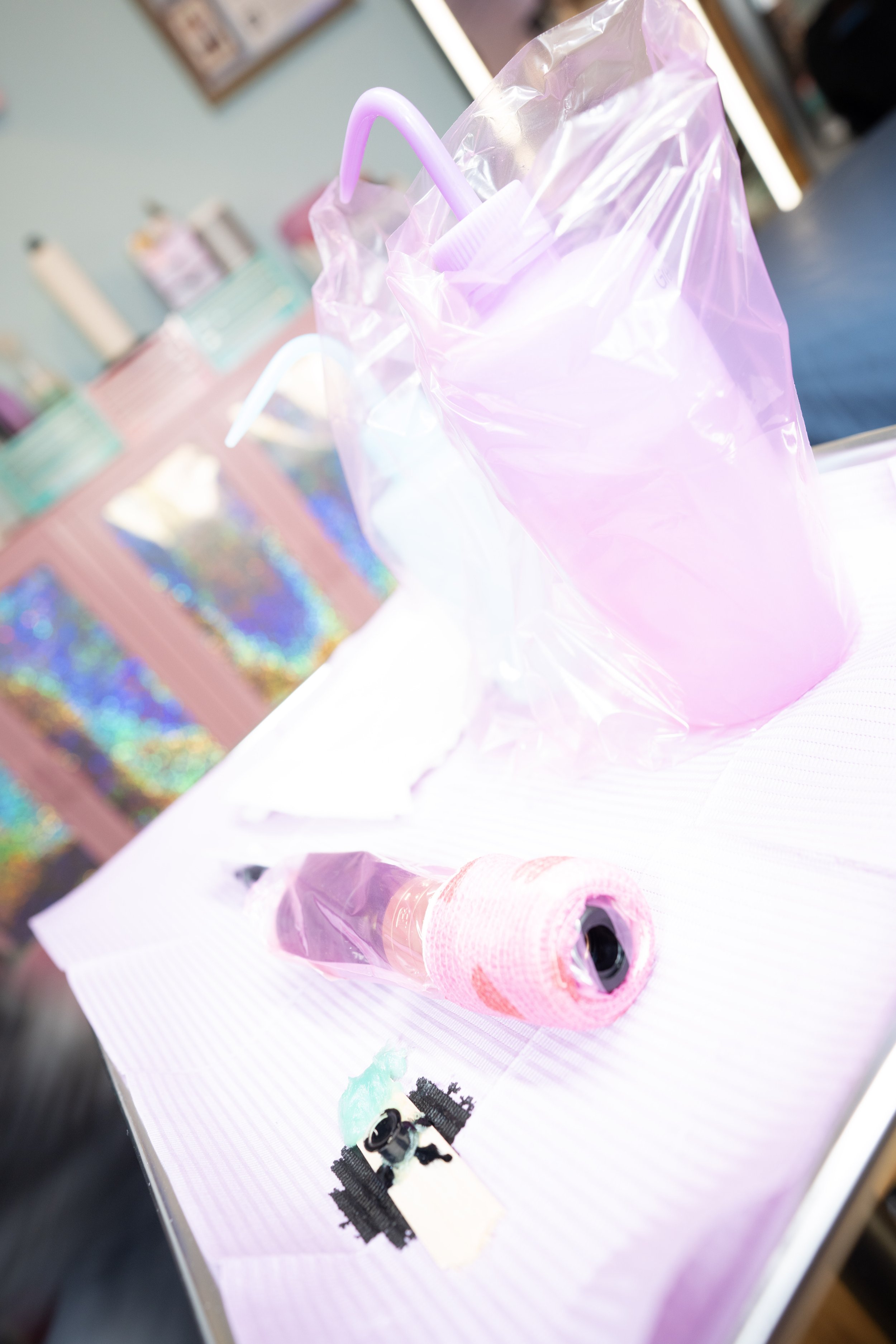 A tattoo instrument tray is set up with tattoo machine, soap bottles, and ink. It is all wrapped  in pretty pastel colors.