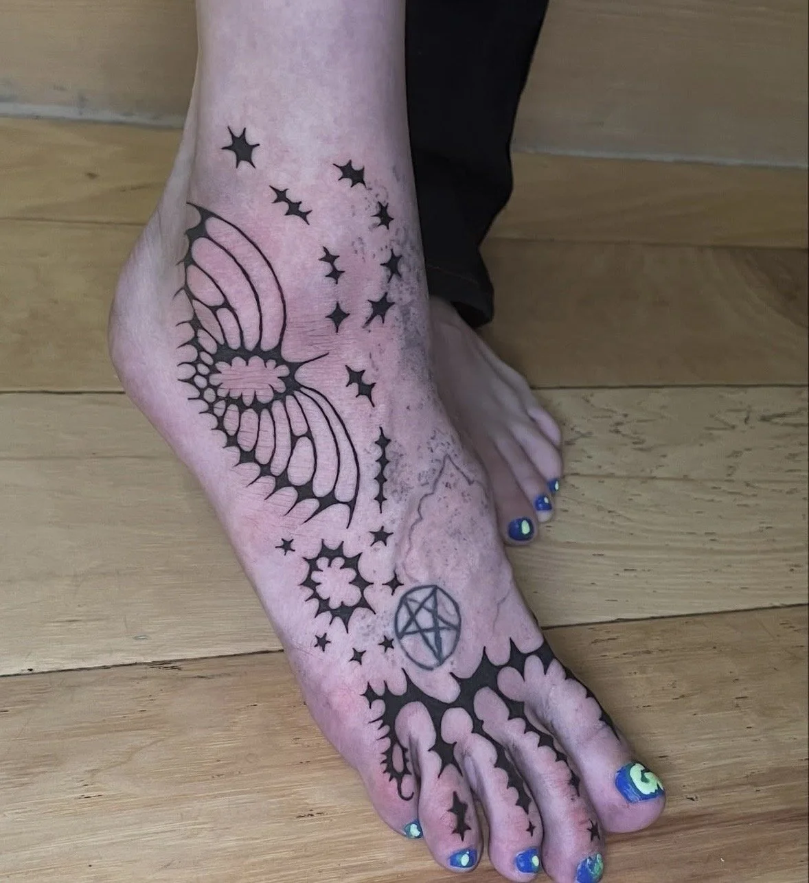 Tattoo of a butterfly, stars, a pentagram, and floral designs on a person's ankle and foot.