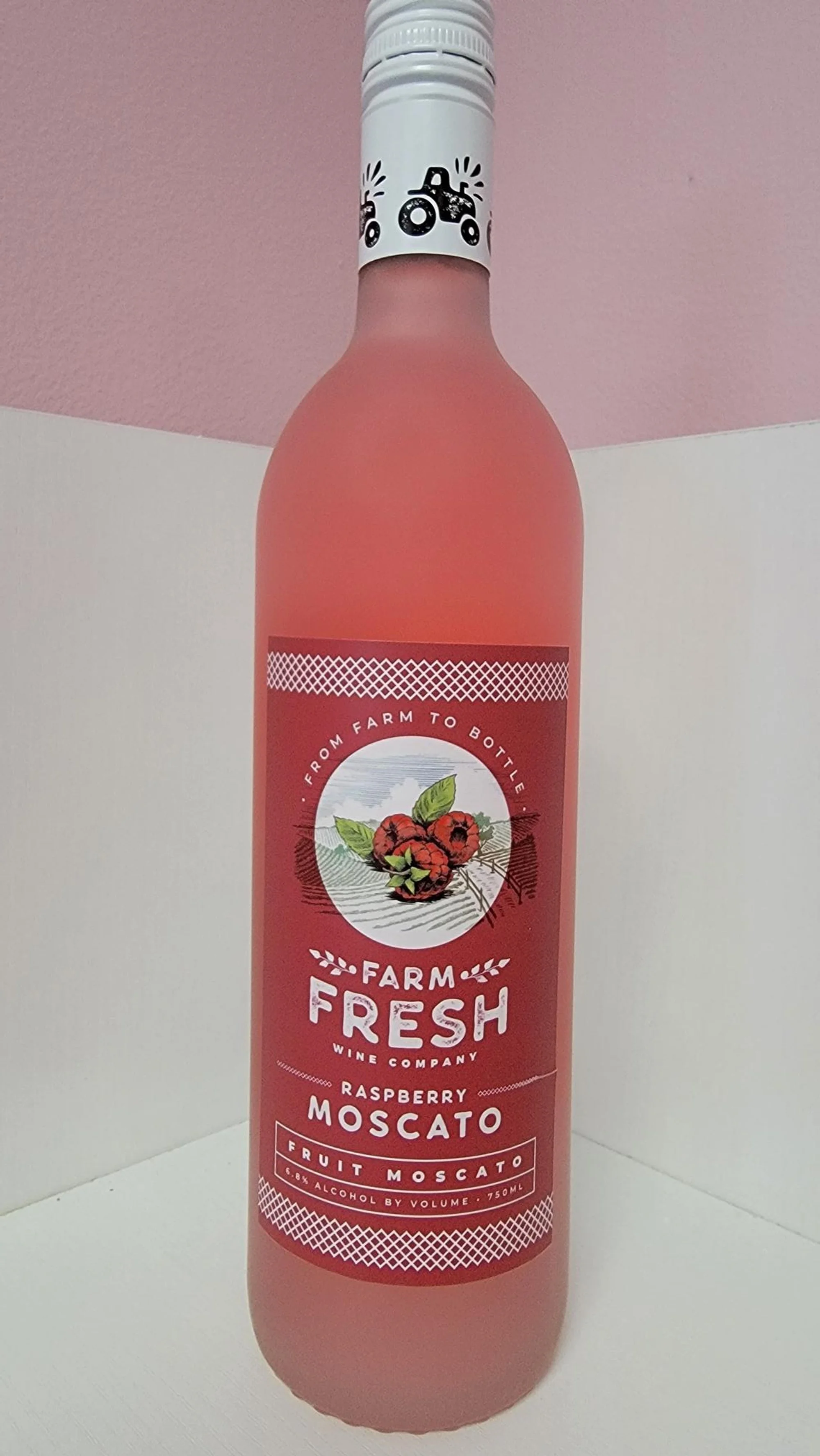 A bottle of Farm Fresh Raspberry Moscato wine with a pink-colored liquid inside, featuring a label with raspberries and the brand name.