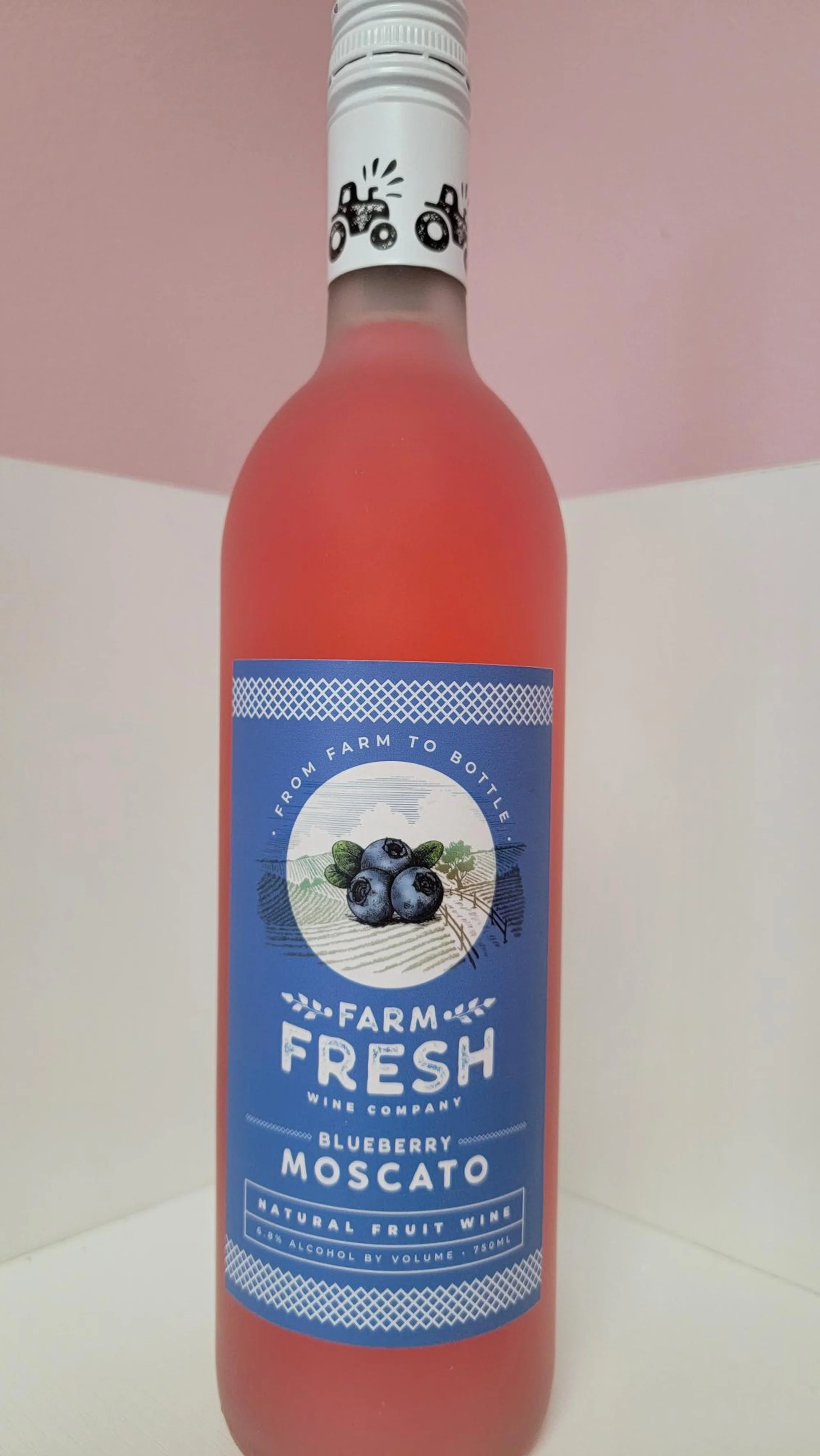 A bottle of Farm Fresh blueberry Moscato wine with a pinkish-red color, featuring a blue label with blueberries and text.