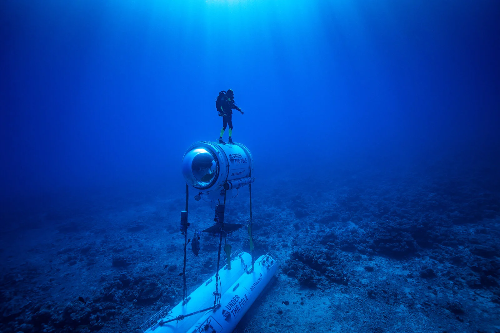An aquanaut from Under The Pole expedition is standing on an underwater capsule in the bottom of the blue pacific ocean