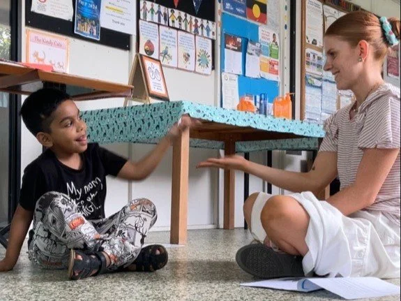 Occupational Therapist Emma Joss working with children and children with disabilities at Lifespan Therapies in Strathpine, North Brisbane. Pictured smiling with a young boy sitting on the floor of a classroom, engaged in a playful hand-clapping game.