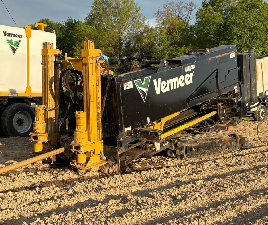 A Vermeer trenching or boring machine on a dirt construction site with trees in the background, featuring black and yellow colors.