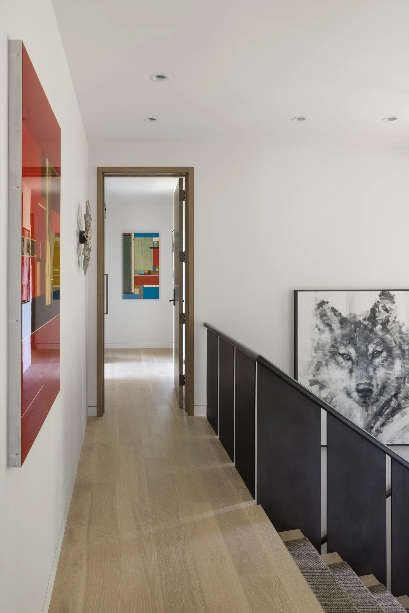Modern hallway with warm white oak hardwood floor, abstract wall art, and architectural staircase.