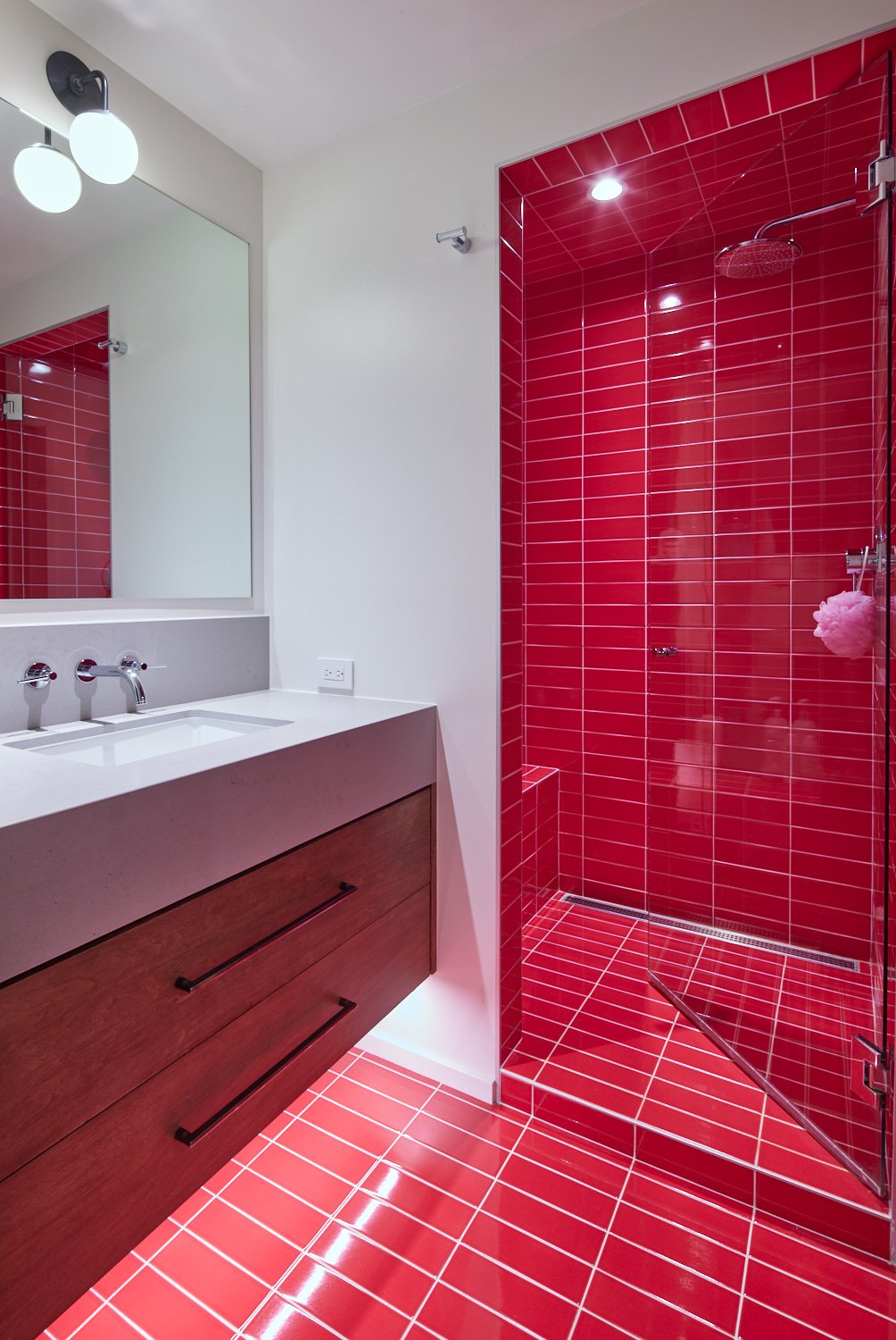 Modern bathroom with red tile shower and floor, white vanity, and large mirror.